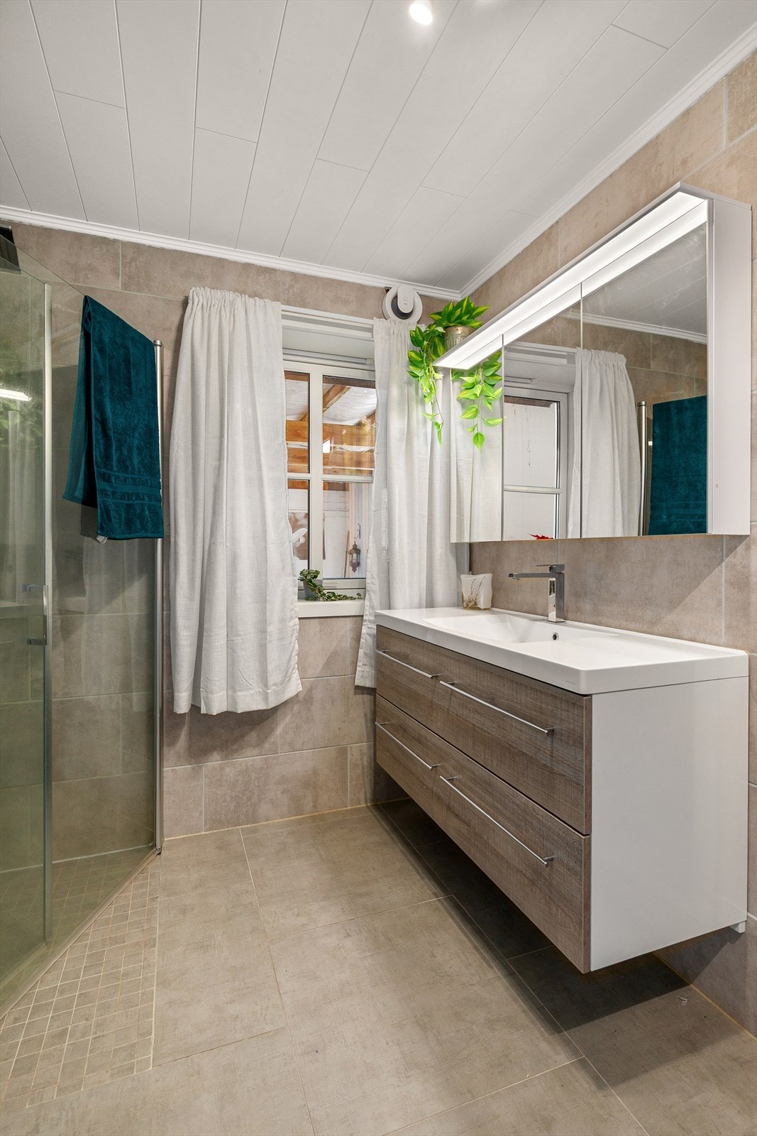 Badet er kombinert bad/vaskerom og er utstyrt med servant med servantskap, veggmontert wc, innfellbare dusjdører, mekanisk avtrekk, opplegg for vaskemaskin samt bereder, vannmåler og stoppekran. Galleribilde