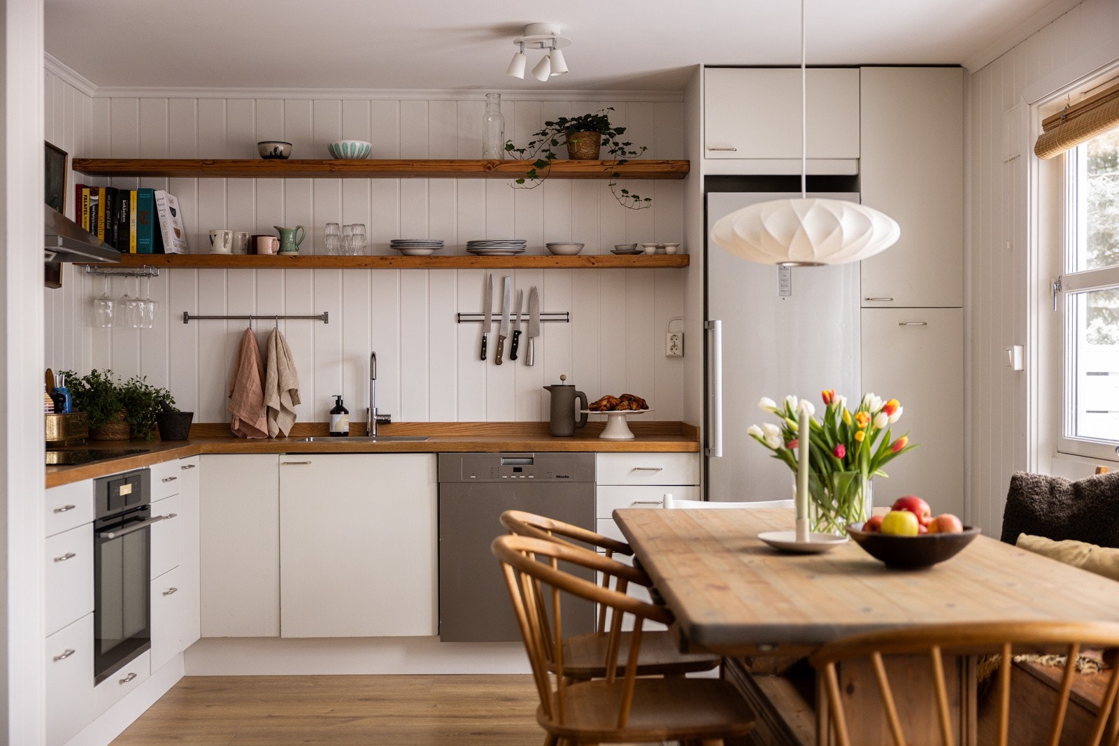 Lys og pen kjøkkeninnredning med glatte fronter malt i 2023 og heltre benkeplate fra 2023 med nedfelt oppvaskkum. Galleribilde