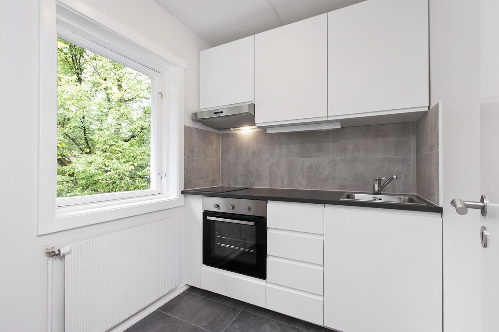 Pent separat kjøkken med mye lys. Hvitevarer som stekeovn, induksjonstopp og kjøl-/fryseskap. Galleribilde