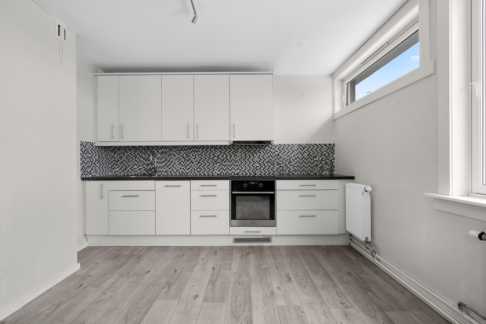 Lys og moderne kjøkkeninnredning med god skap- og benkeplass. Innredningen har hvite glatte fronter og laminert benkeplate med nedfelt oppvaskkum. Galleribilde