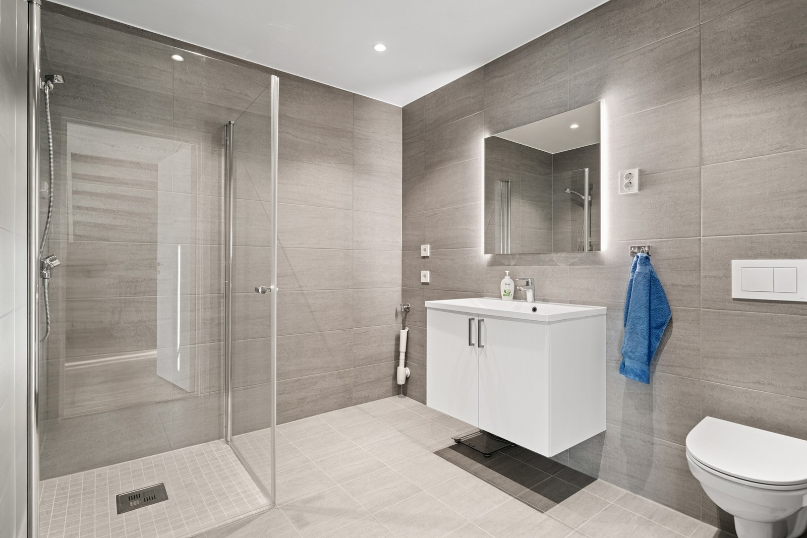 Flislagt bad med gulvvarme, dusj, vegghengt toalett og innredning med servant, samt opplegg til vaskemaskin og tørketrommel. Praktisk plassert i tilknytning til soverommene. Galleribilde