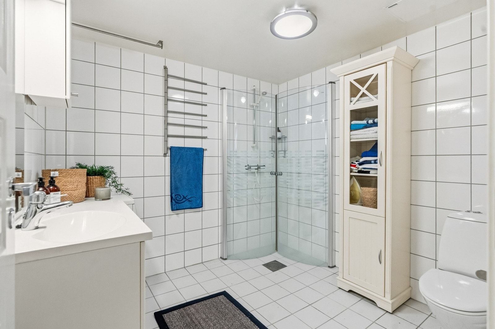 Badet har varmekabler i gulvet og er flislagt med hvite fliser på både gulv og vegger, noe som gir et rent og tidløst uttrykk. Galleribilde