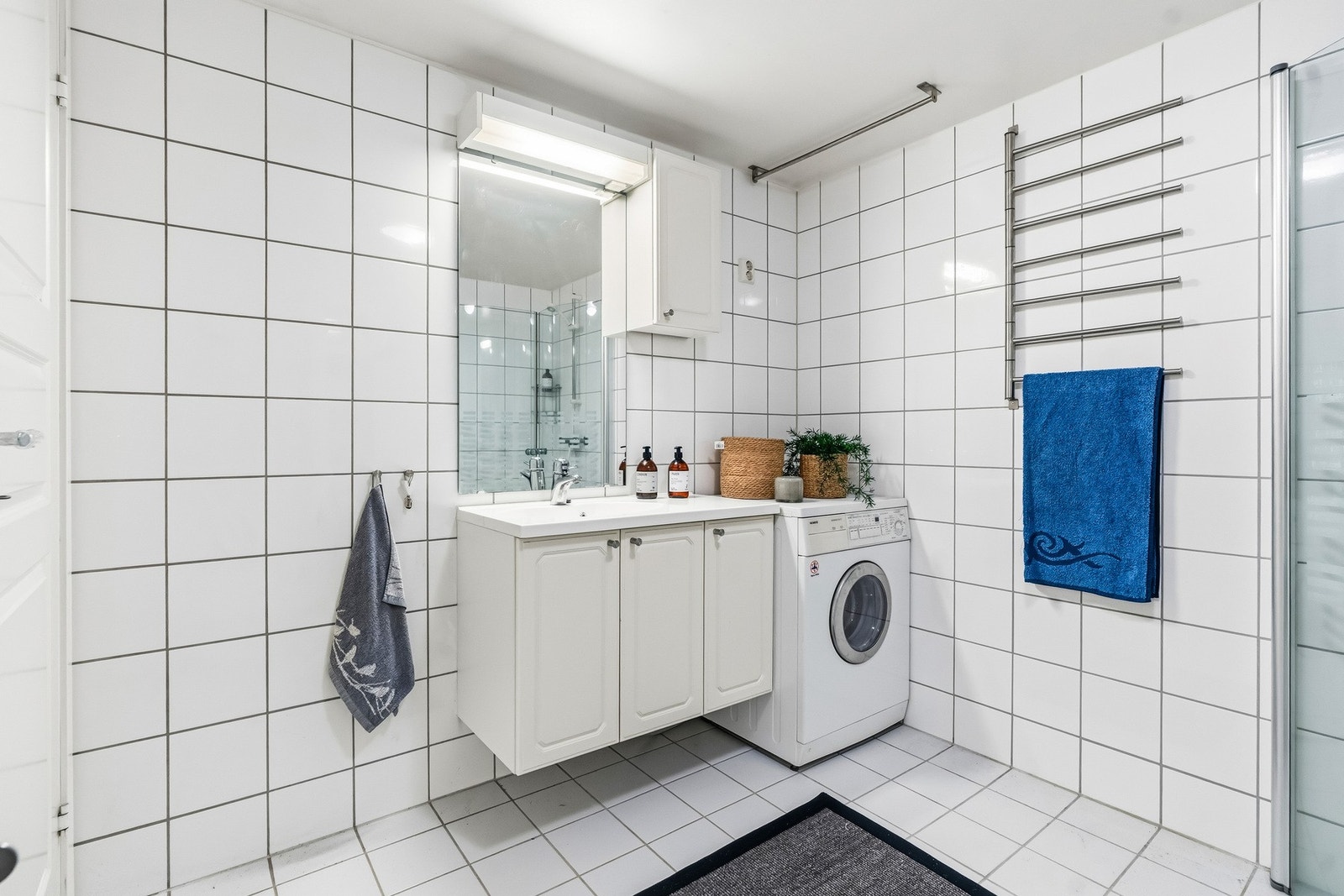 Baderomsinnredningen består av benkeskap og veggskap med profilerte fronter og servant. Videre er badet utstyrt med gulvstående klosett og dusj med innfellbare dører i herdet glass. Det er også opplegg for vaskemaskin. Galleribilde