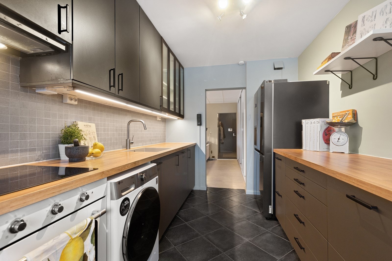 Innredning bestående av laminat benkeplate, planlimt vask og ettgreps kjøkkenarmatur med svingfunksjon. Mellom benkeplate og overskap er det fliser, kullfilter avtrekk. Galleribilde