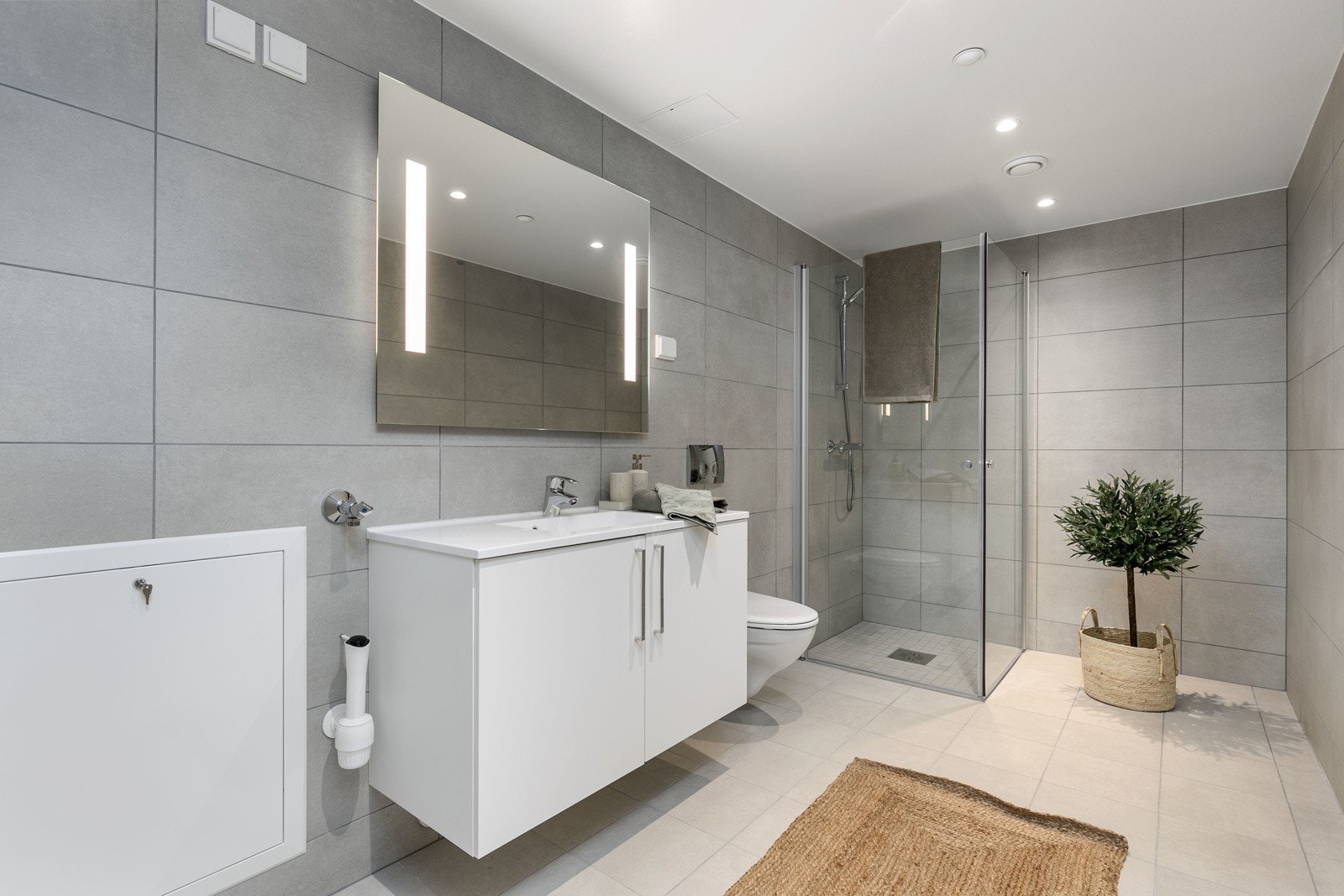 Delikat flislagt bad med vegghengt toalett, dusjsone med innfellbare dører samt servant med skapinnredning. Galleribilde