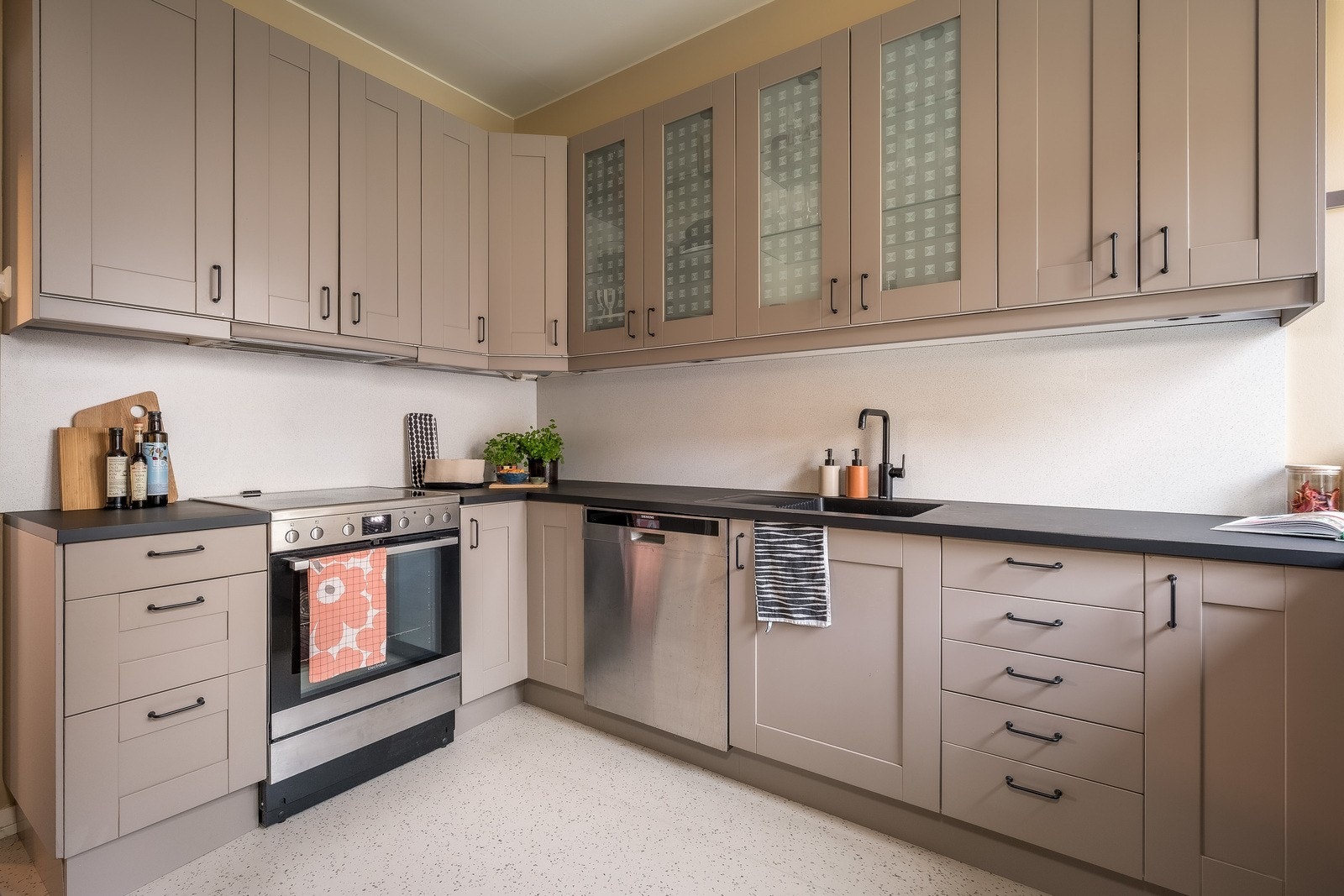 Innredningen er utført med malte fronter, herunder to overskap med glassfronter, samt laminate benkeplater med kjøkkenarmatur og underlimt oppvaskkum. Galleribilde