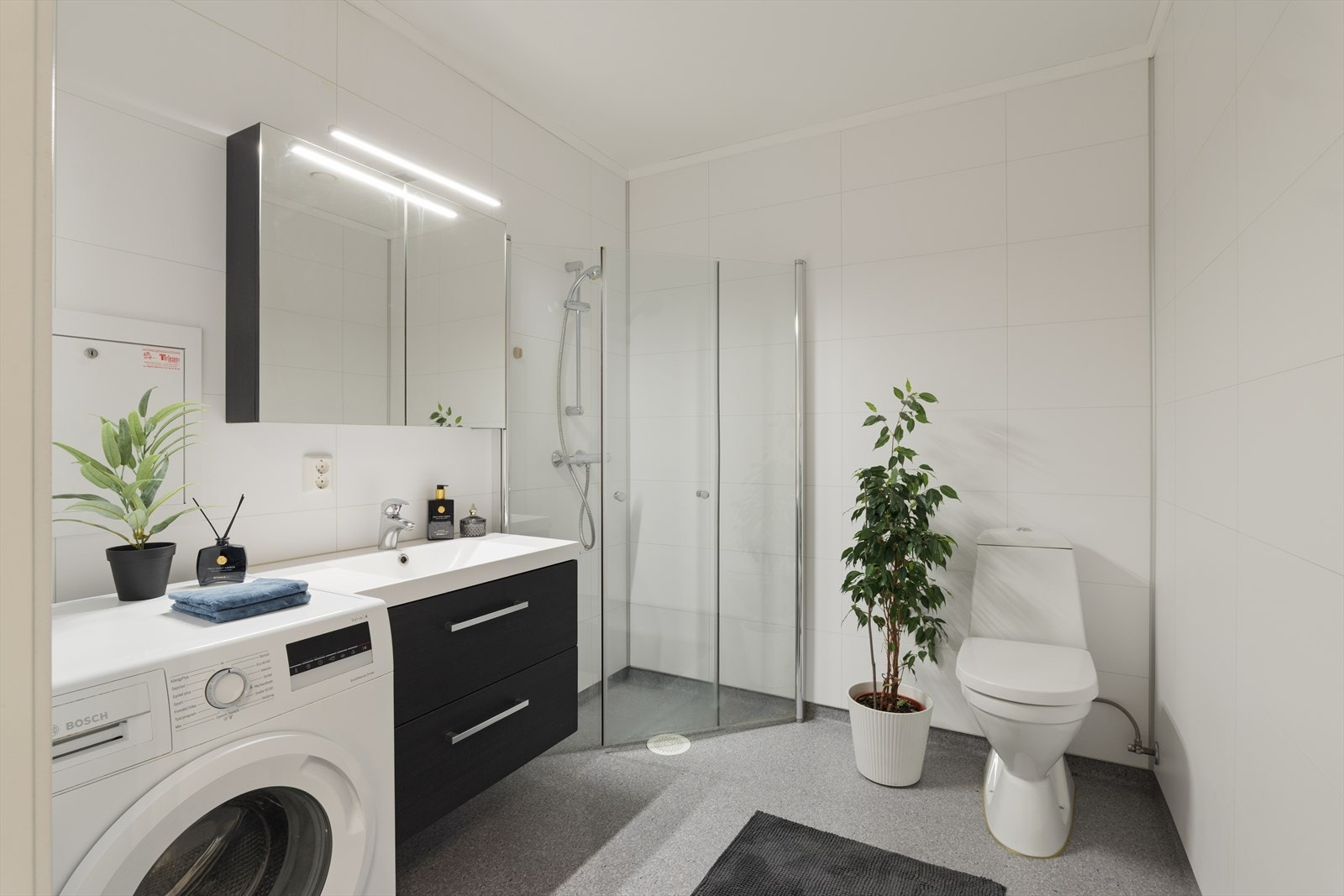 Badet er innredet med servant med skuffer, innfellbare dusjvegger, gulvmontert toalett og opplegg for vaskemaskin. Galleribilde