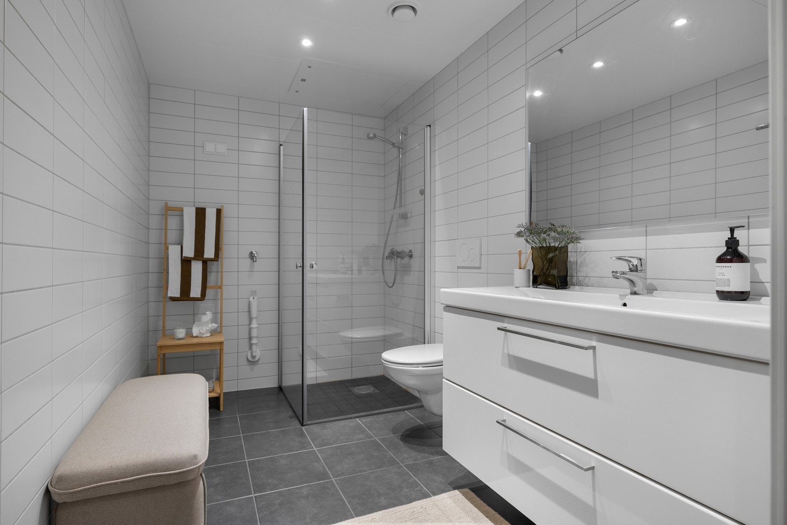 Badet på vei inn til stua er praktisk og pent. Flislagt på gulv og vegger. Innredning med heldekkende servant og lagring i kolonialskuffer. Badet er i underkant av 6m2 Galleribilde