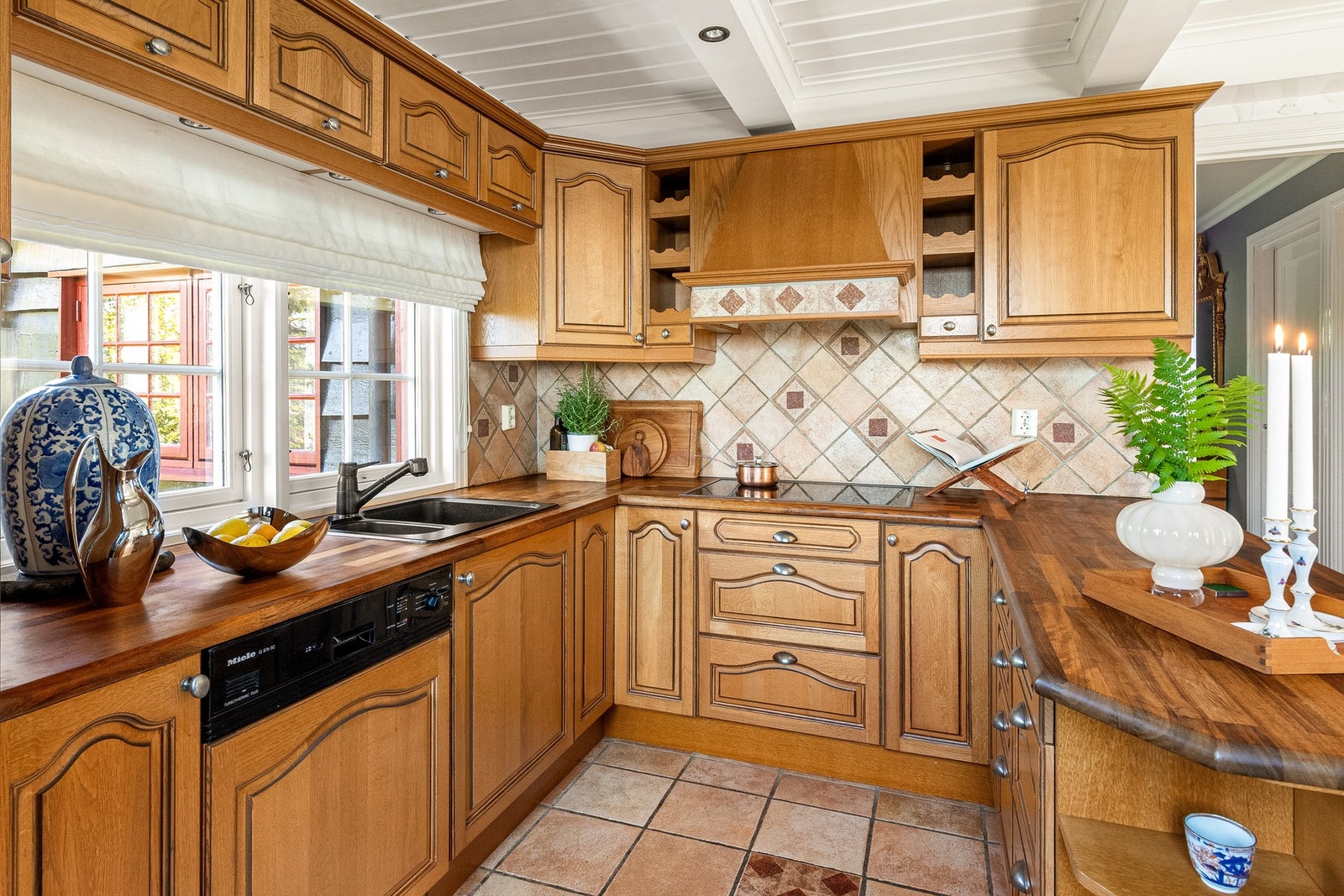 U-formet kjøkken med rikelig med arbeids- og skapplass, fliser på vegg over benkeskap. Heltre benkeplate med nedfelt kum i kompositt Galleribilde