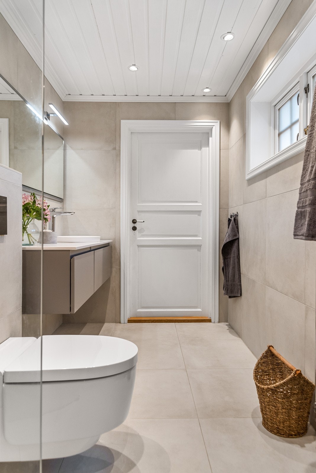 Badet er videre innredet med toalett, bred skuffeseksjon med nedfelt servant, stort speil med lys og håndkletørker på vegg. Galleribilde