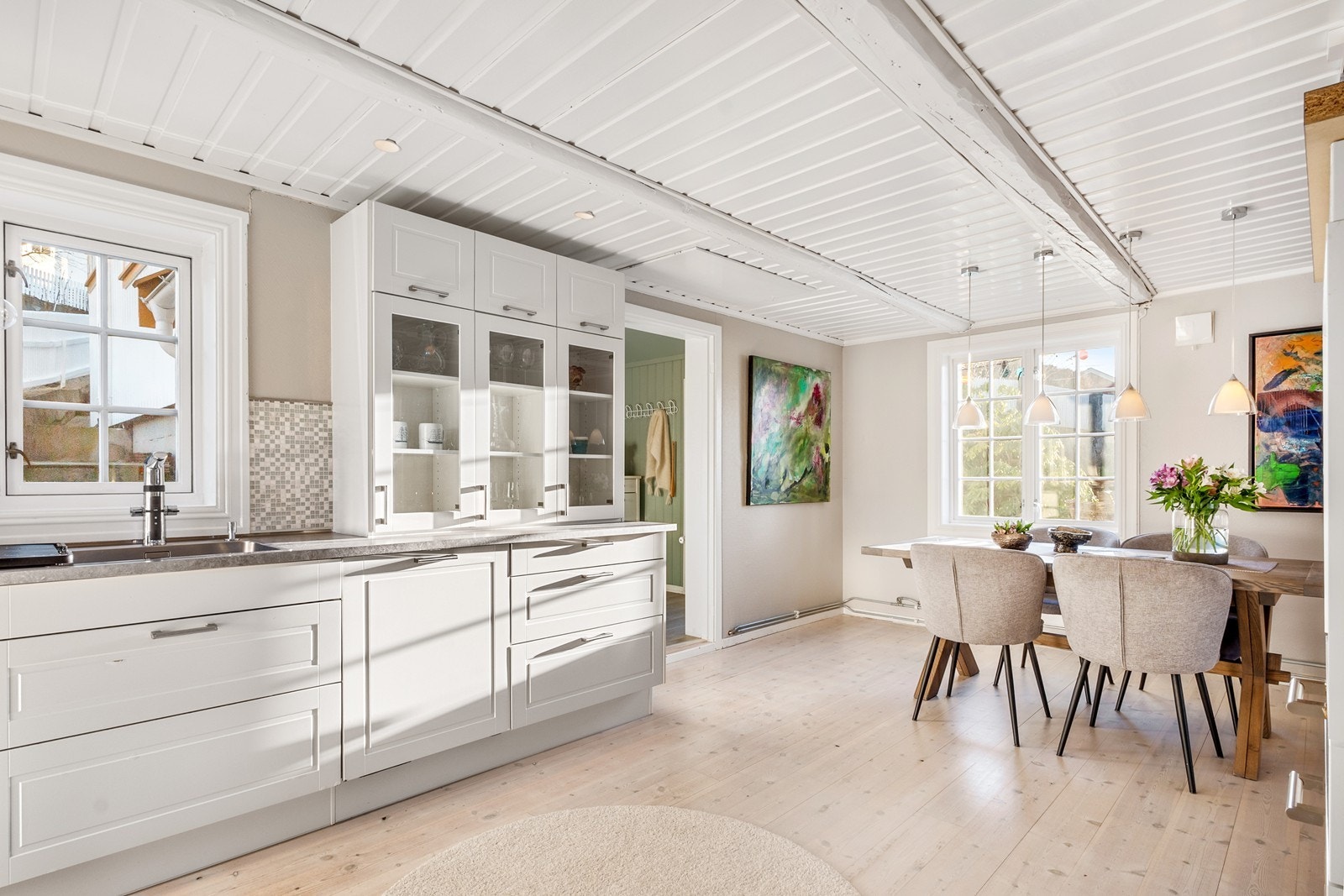 Kjøkkenet med spisestue er et stort og lyst rom med heltregulv og paneltak kombinert med slettmalte vegger og moderne innredning. Galleribilde