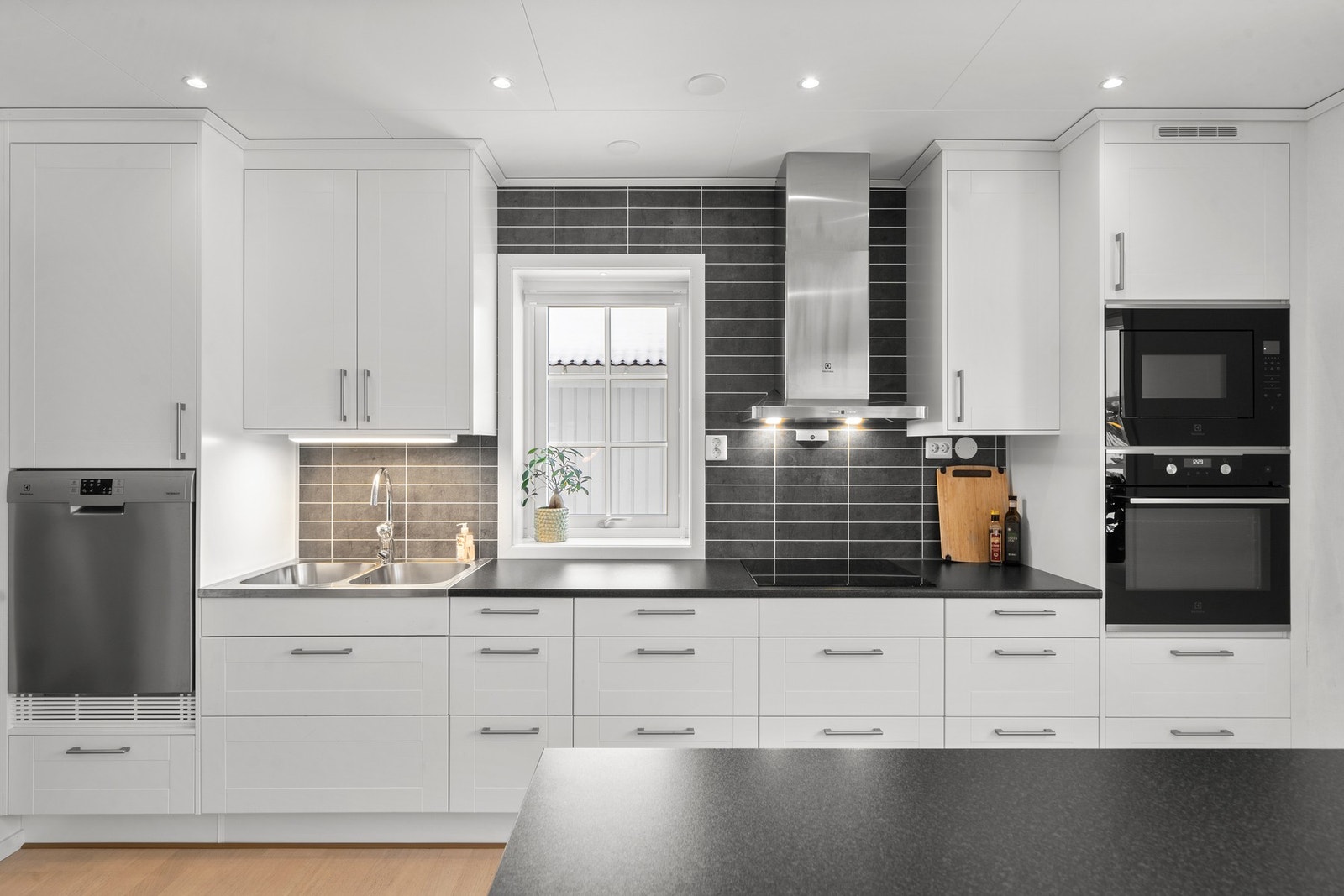 Praktisk med mørke flisimitasjonsplater i benkeryggen og belysning under overskap i tillegg til downlights i himlingen. Galleribilde