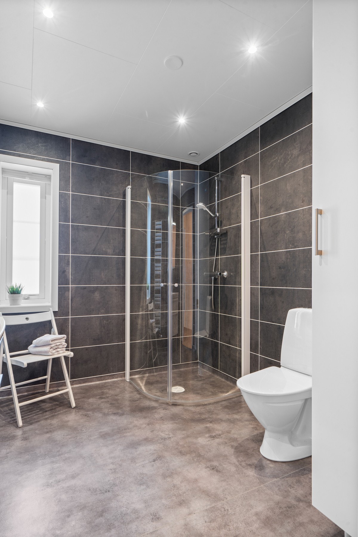 Moderne baderominnredning med skuffer og heldekkende servant, speilskap med belysning over. Baderommet er også utstyrt med dusjhjørne med glassdører og gulvstående toalett. Galleribilde