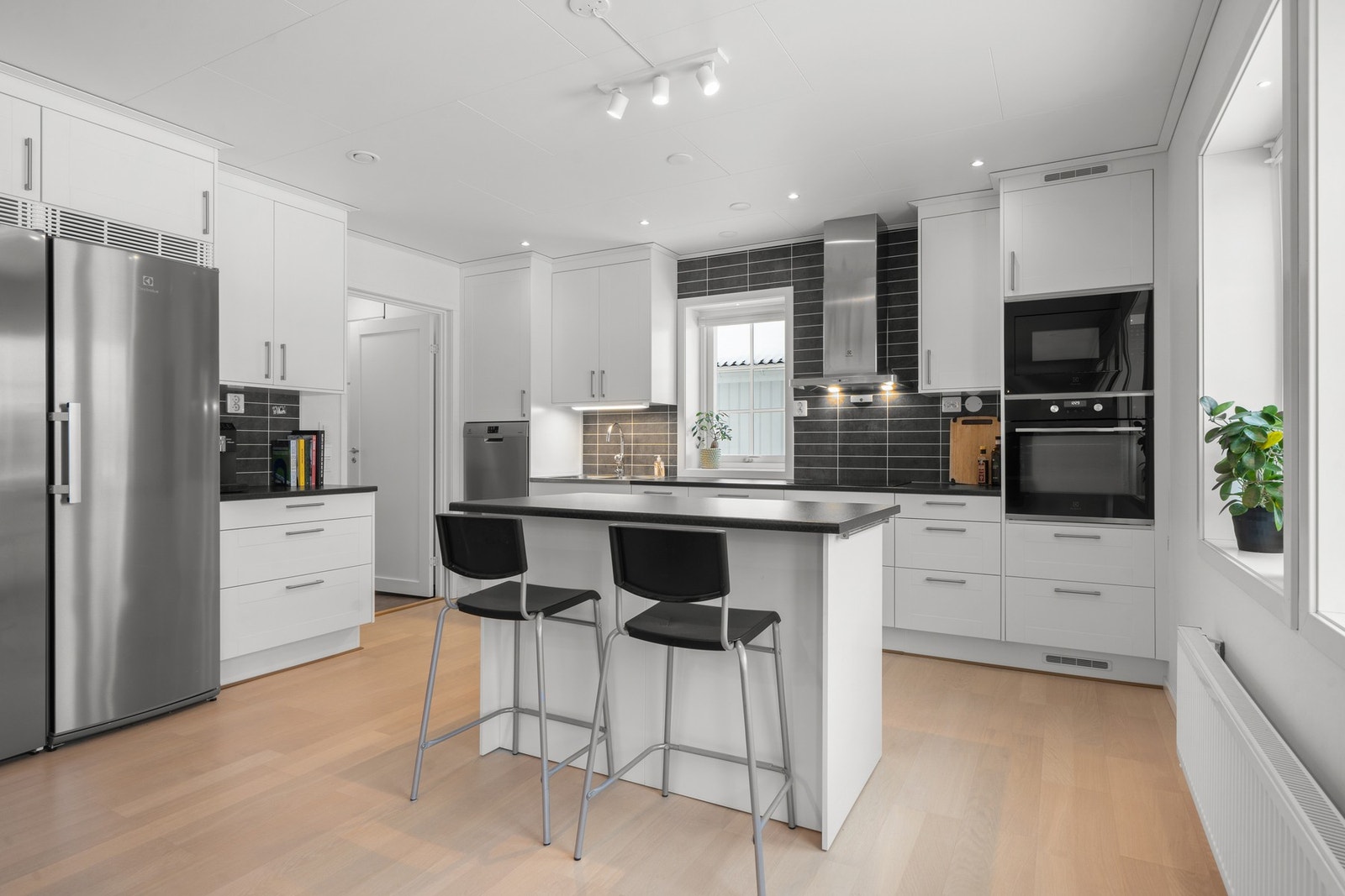 Lys og moderne kjøkkeninnredning fra 2020 med hvite glatte fronter og laminert benkeplate med nedfelt platetopp. Galleribilde