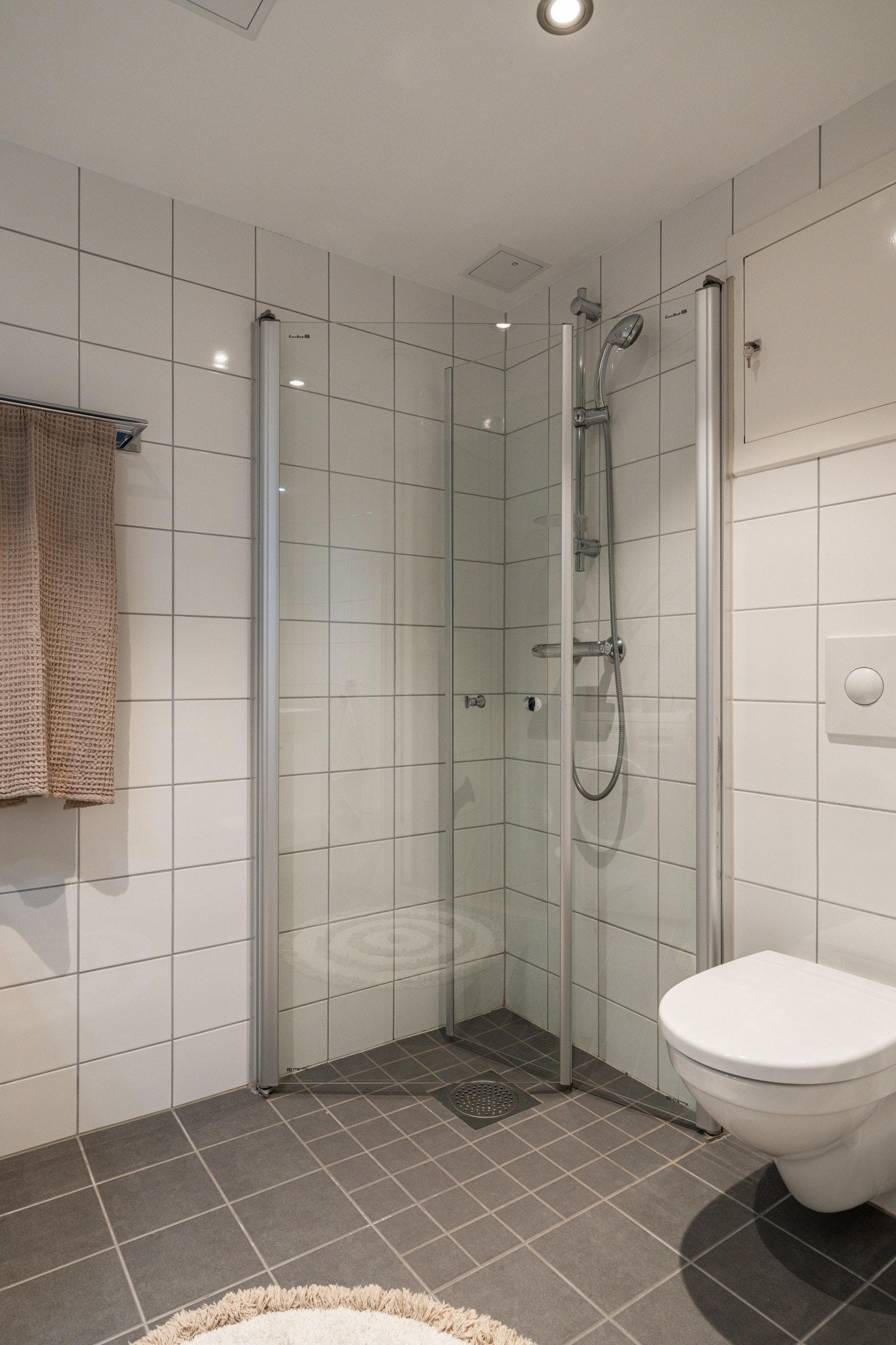 Baderommet har lysegrå fliser på gulv, elektriske varmekabler, lyse fliser på veggene og avtrekk via balansert ventilasjon. Galleribilde