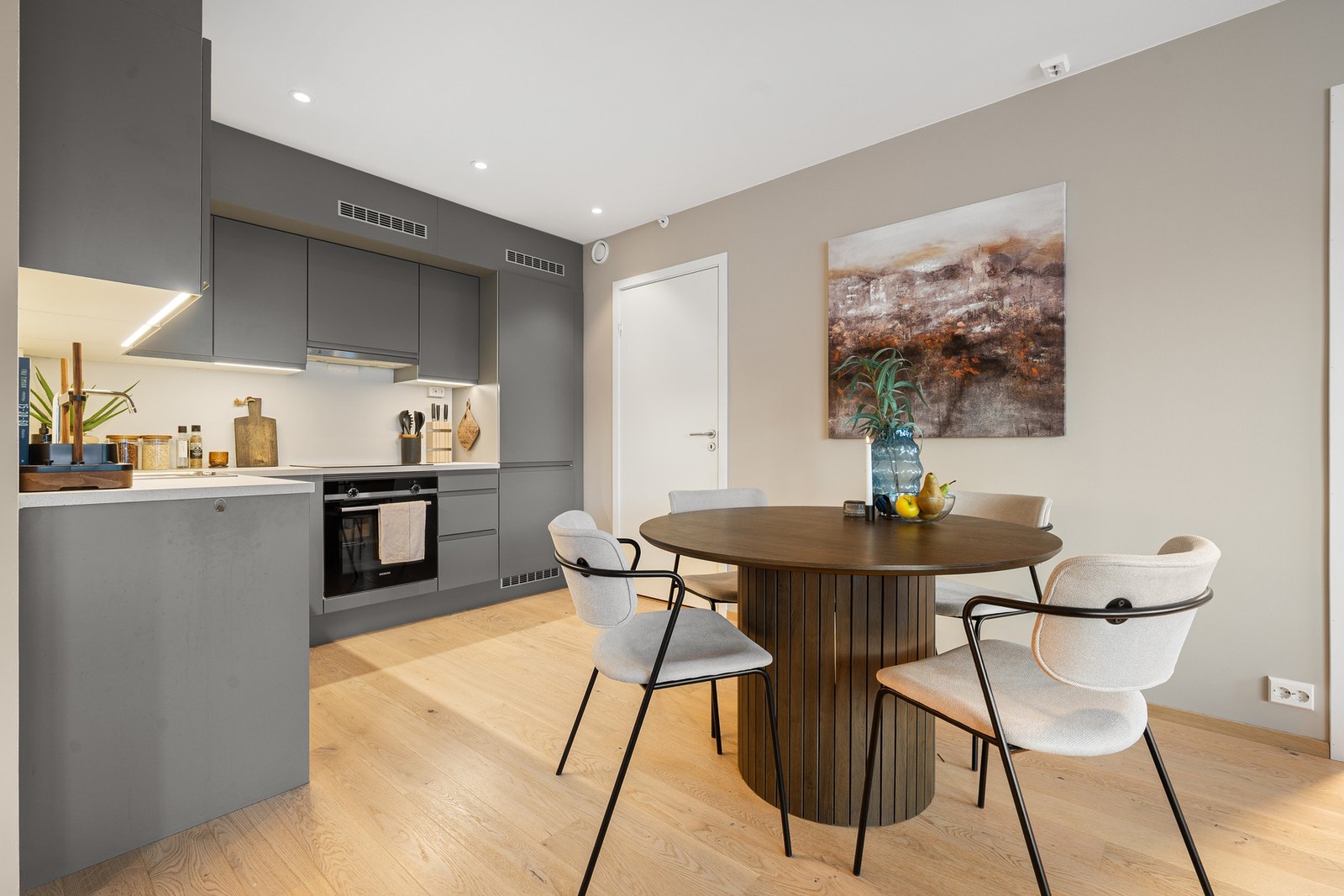 Pent kjøkken med grå slette fronter og integrerte hvitevarer. Praktisk bod innenfør døren til høyre. Galleribilde