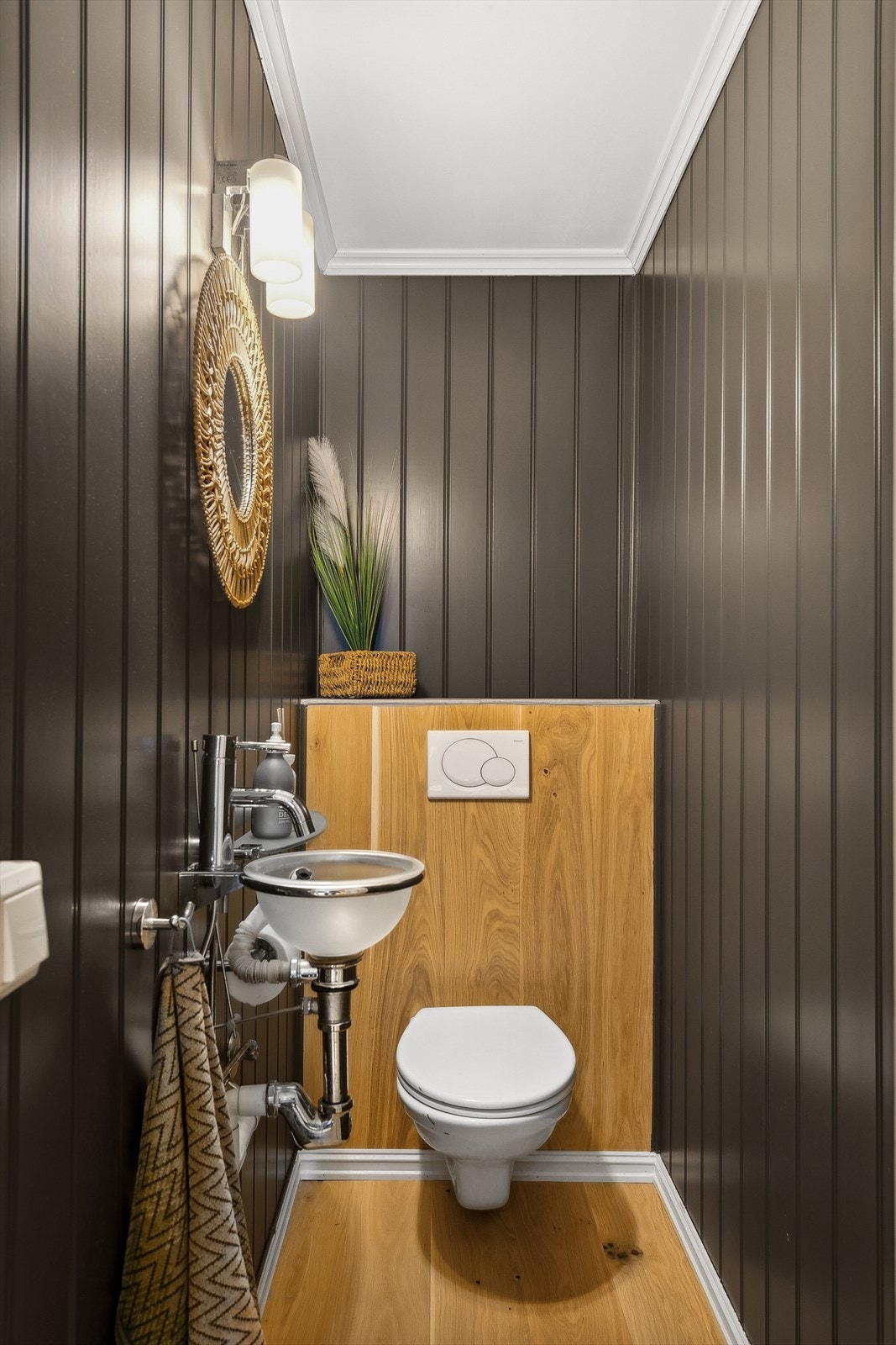 Toalettrom med parkett på gulv. Sanitærutstyr bestående av en liten vask og vegghengt klosett. Galleribilde