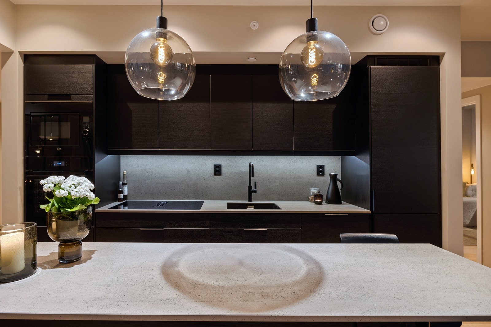 Ekstra bred induksjon koketopp med integrert benkeventilator koblet mot avtrekksanlegge. Iintegrert stekeovn, microovn, oppvaskmaskin og kjøl-/fryseskap. Oppvaskmaskin og kjøl-/fryseskap er fra Miele, øvrige hvitevarer er fra AEG Galleribilde