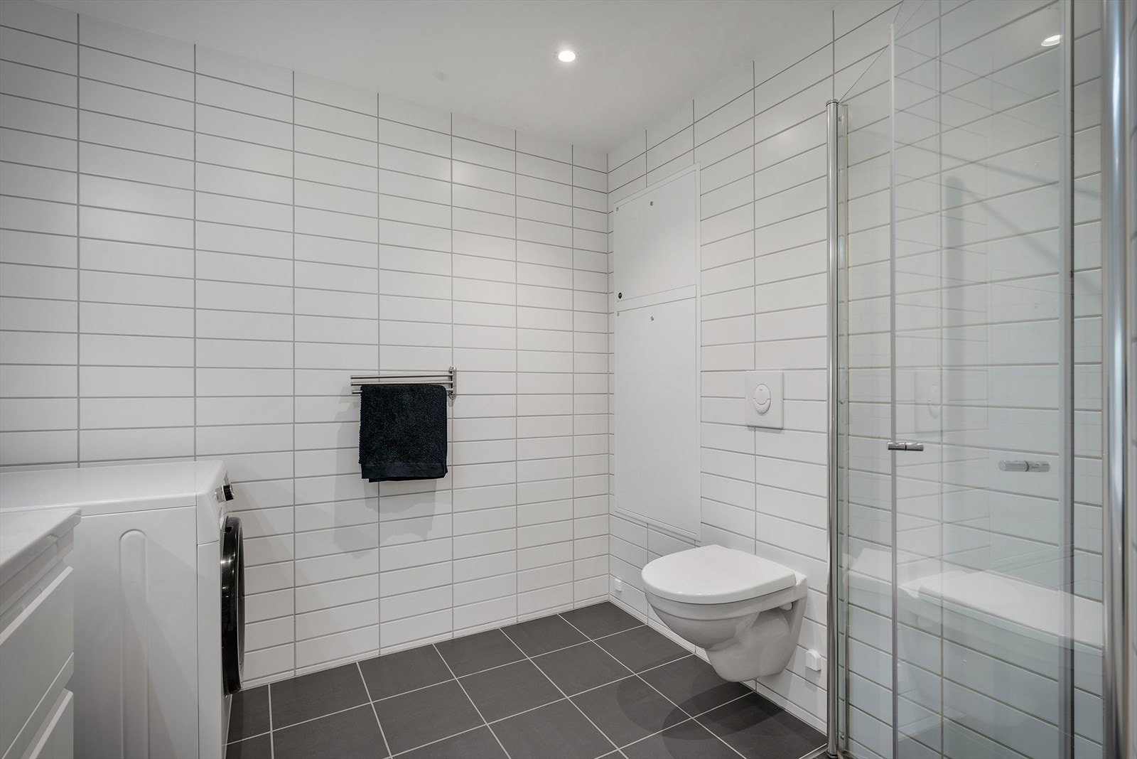 Badet er innredet med baderomsmøbel med heldekkende servant, speilskap m/ belysning, vegghengt toalett, dusj med glassdører og opplegg for vaskemaskin. Galleribilde