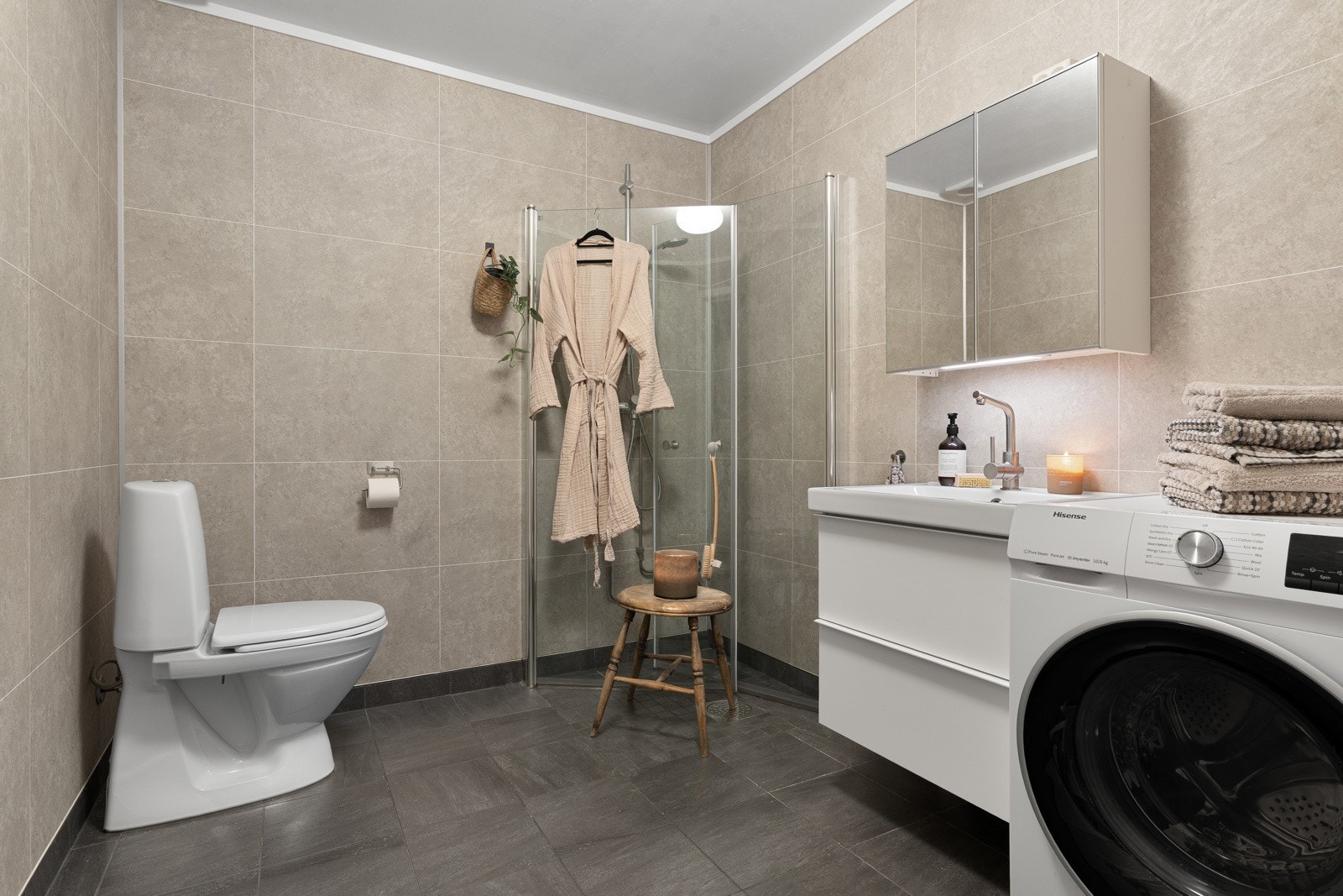 Badet framstår moderne, med flislagt gulv med gulvvarme og praktisk dusjhjørne med innfellbare glassdører.