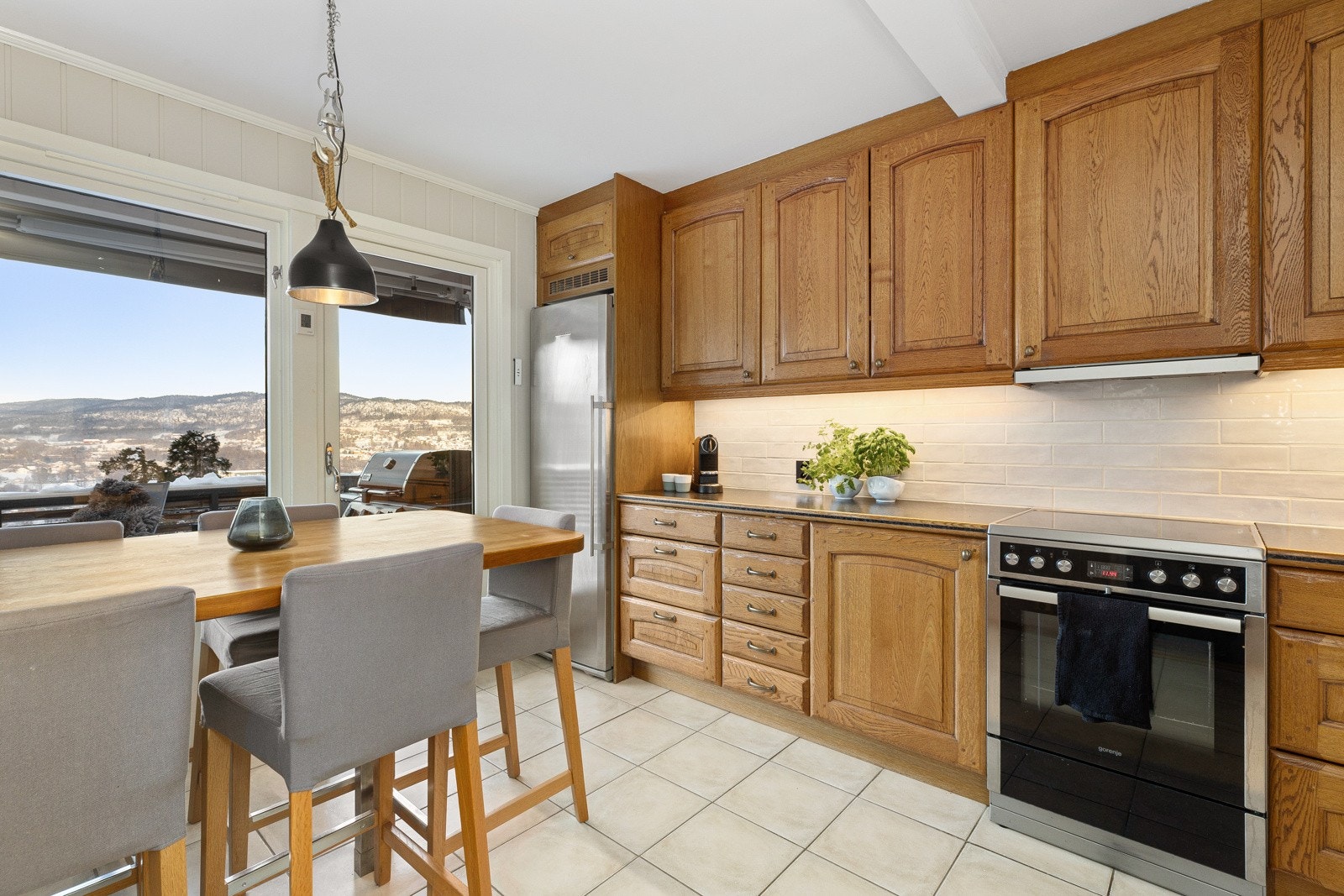 Romslig spisekjøkken av heltre eik med profilerte fronter og laminat benkeplate med nedfelt kum i stål. Galleribilde