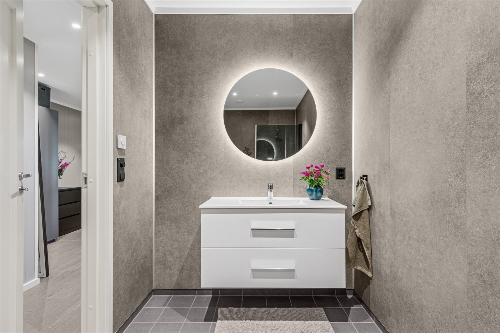 Delikat og funksjonelt baderom med vegghengt toalett, dusjhjørne med dusjdører, og servant med skuffeinnredning i lys utførelse. Galleribilde