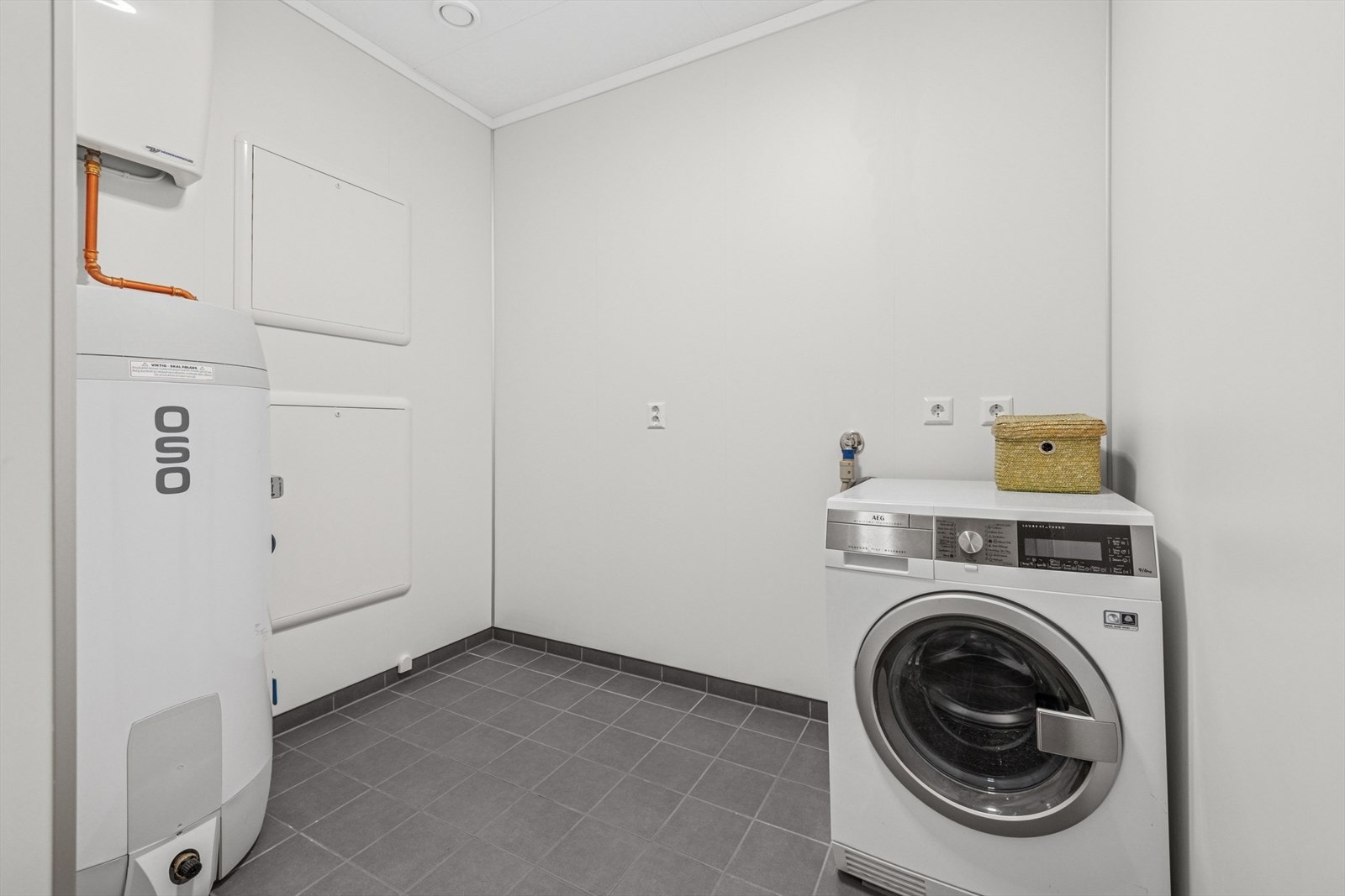 Praktisk vaskerom med opplegg for vaskemaskin. Gulvet er flislagt og har varme, mens veggene er kledd med våtromsplater og taket med himlingsplater. Galleribilde