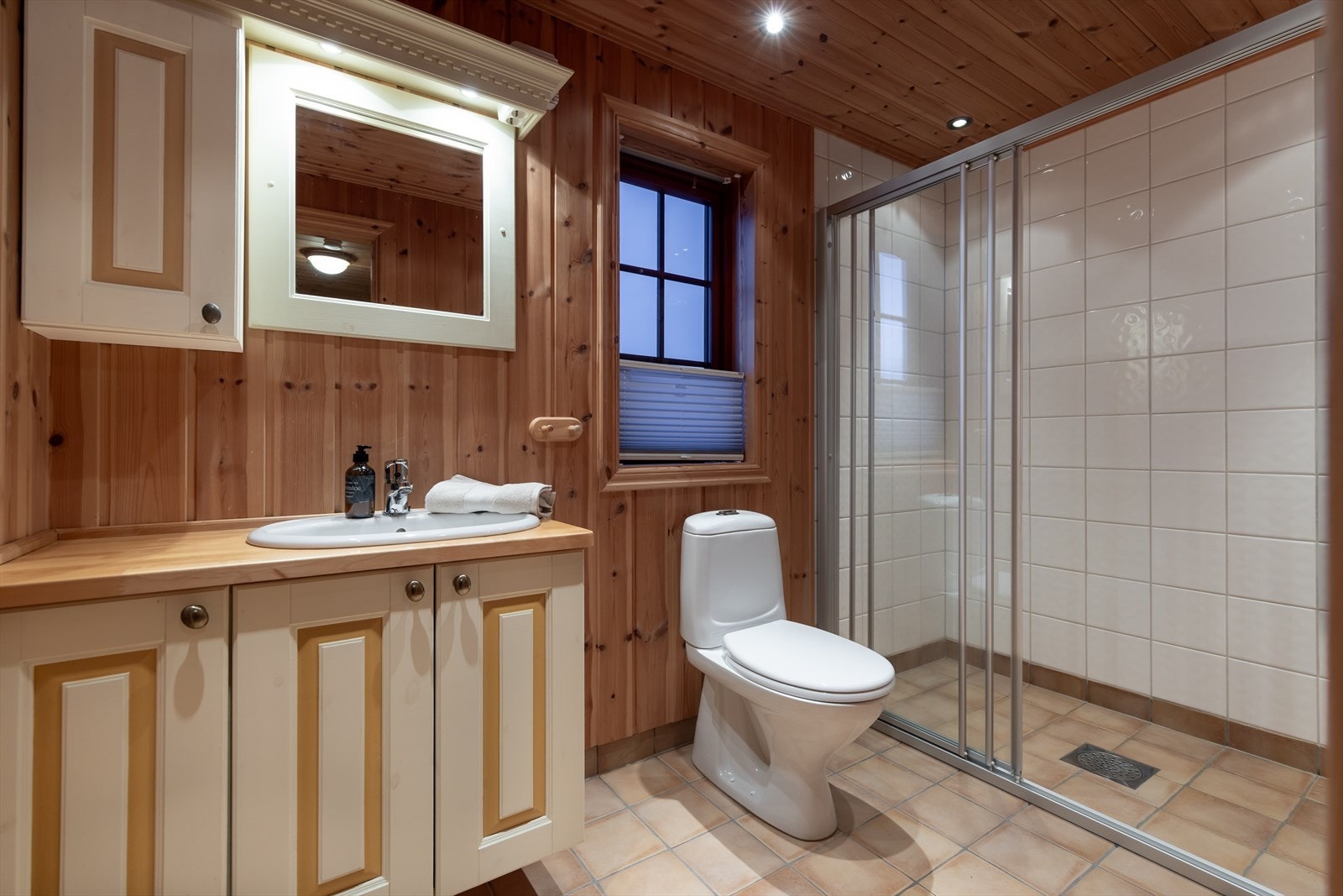 Romslig baderom med flislagt gulv, panelte vegger, baderomsinnredning, wc og stor dusjnisje. Galleribilde
