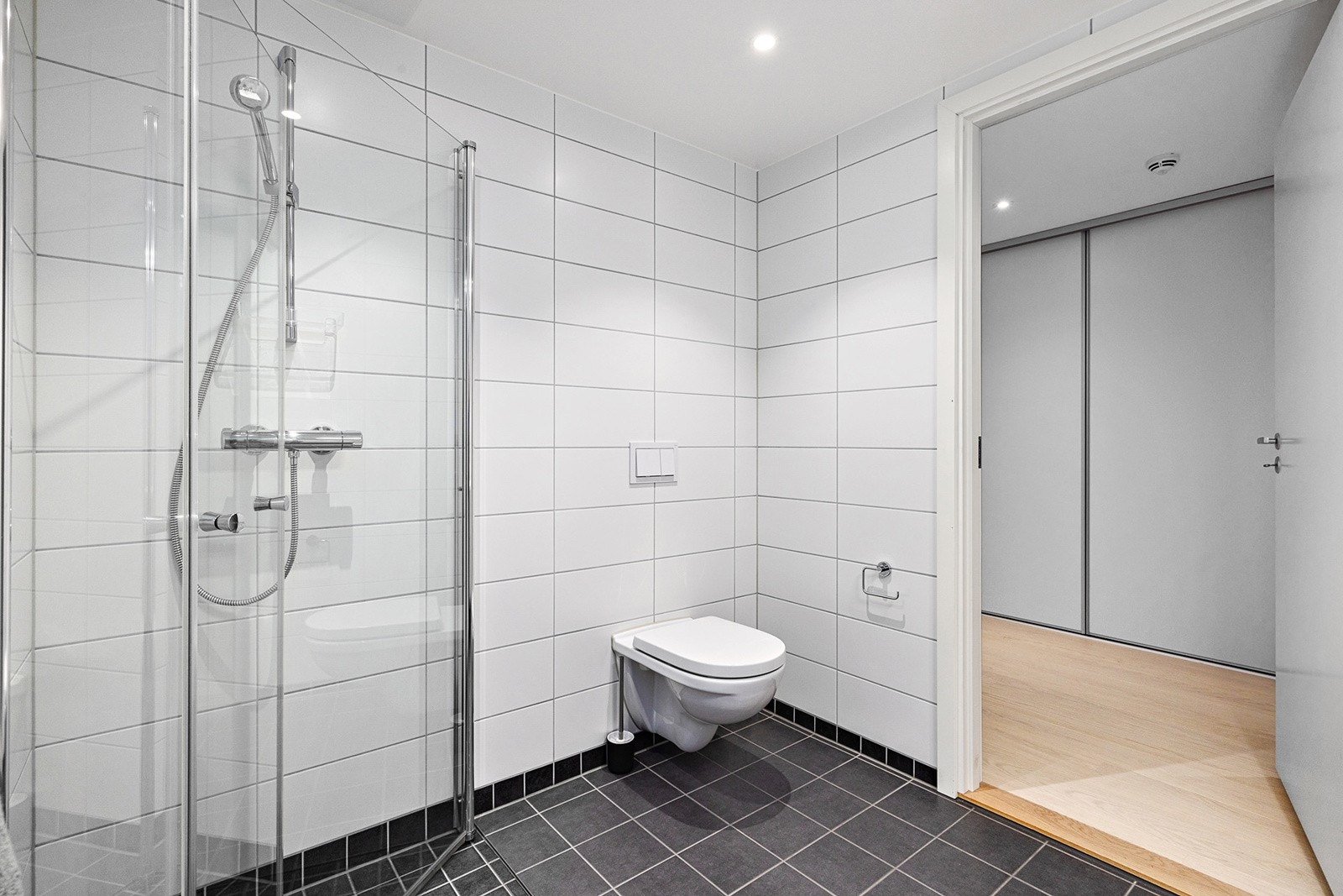 Inn- utadslående dusjvegger, servant med underskap, overskap med speilfronter og overlys, veggklosett og opplegg for vaskemaskin. Galleribilde