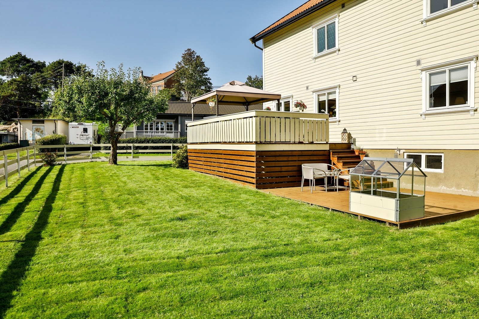 Hagen er lettstelt, solfylt dagen gjennom sommerstid og pent rammet inn av gjerde oppført i 2018. Plattingen ble anlagt i 2010. Bildet er tatt i 2019 og viser eiendommen sommerstid. Galleribilde