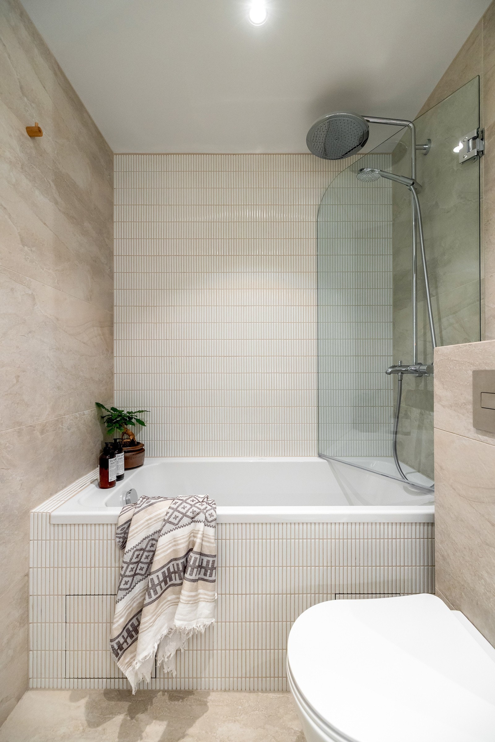 Badet er innredet med innfliset badekar i mosaikk med halv glassvegg, håndholdt- og regnfallsdusj, samt veggmontert toalett Galleribilde