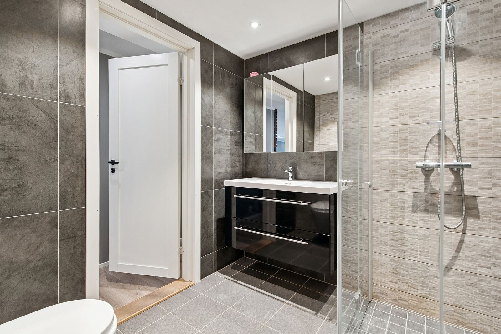 Lekkert flislagt bad med vaskemaskin og godt med lagringsplass i servant og speilskap Galleribilde