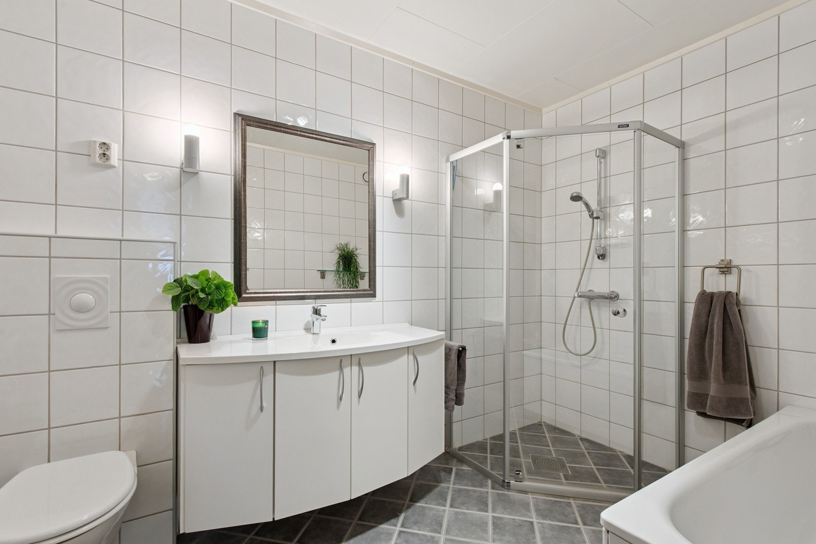 Stort fliselagt bad med dusjhjørne, badekar og vegghengt toalett. Galleribilde