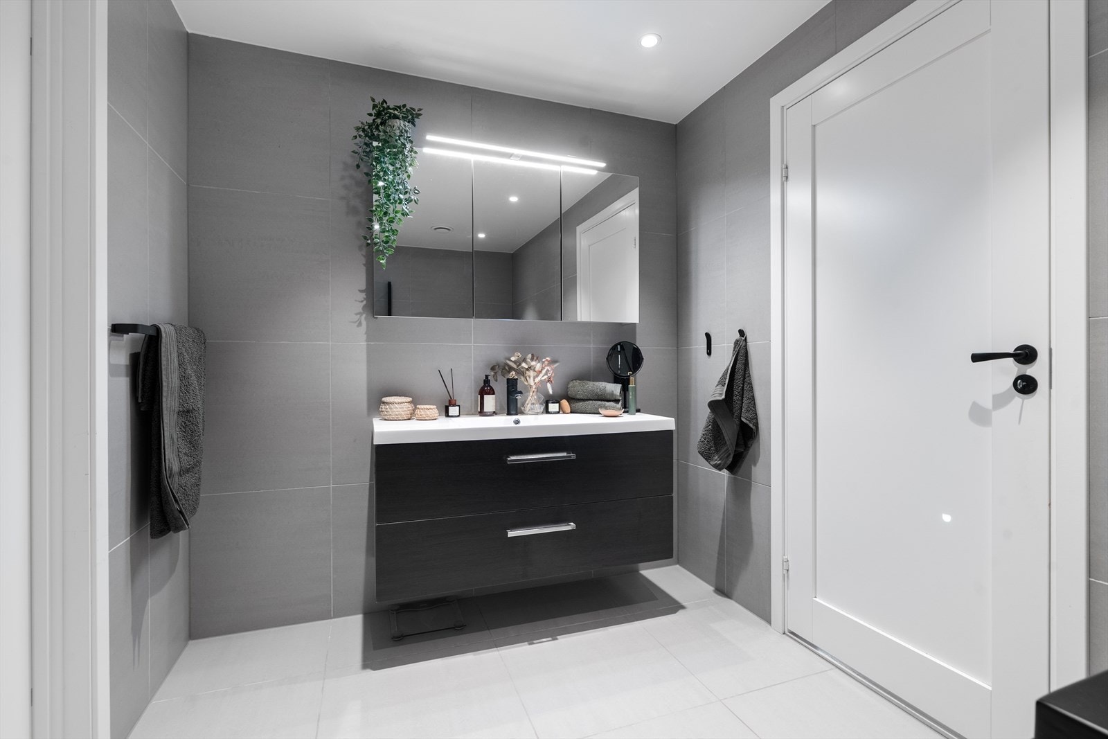 Mørk og pen innredning med fronter i slett utførelse og heldekkende servant, overskap med speilfronter og overlys. Galleribilde