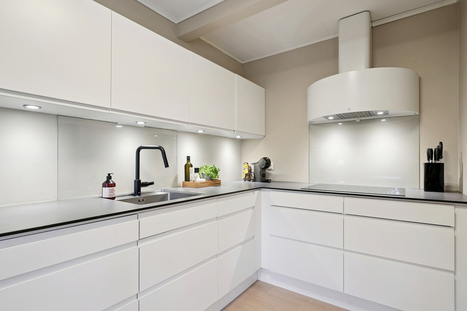 Glassplater på vegg bak oppvaskkum og platetopp, samt belysning under overskap. Galleribilde