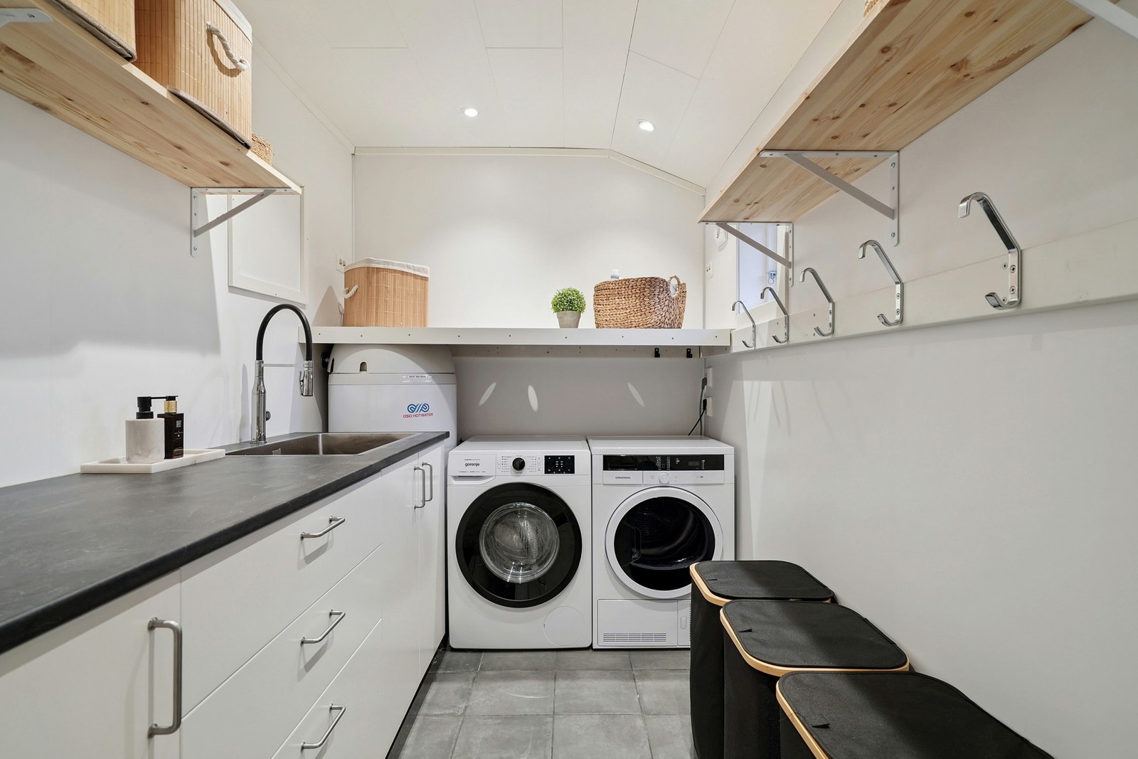 Praktisk vaskerom med flislagt gulv og elektriske varmekabler. Innredet med opplegg for vaskemaskin, hyller og innredning med skap og skuffer. Galleribilde