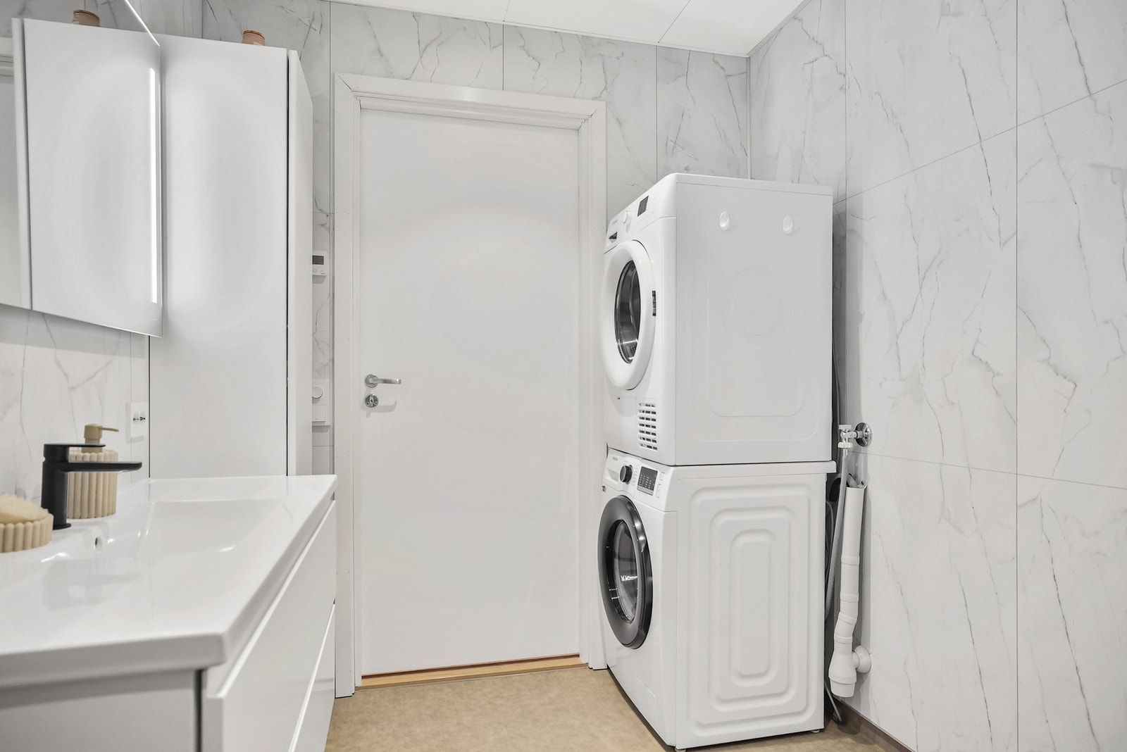 Baderommet inneholder vegghengt høyskap, dusjhjørne med dører, vegghengt toalett og opplegg til vaskemaskin. Galleribilde