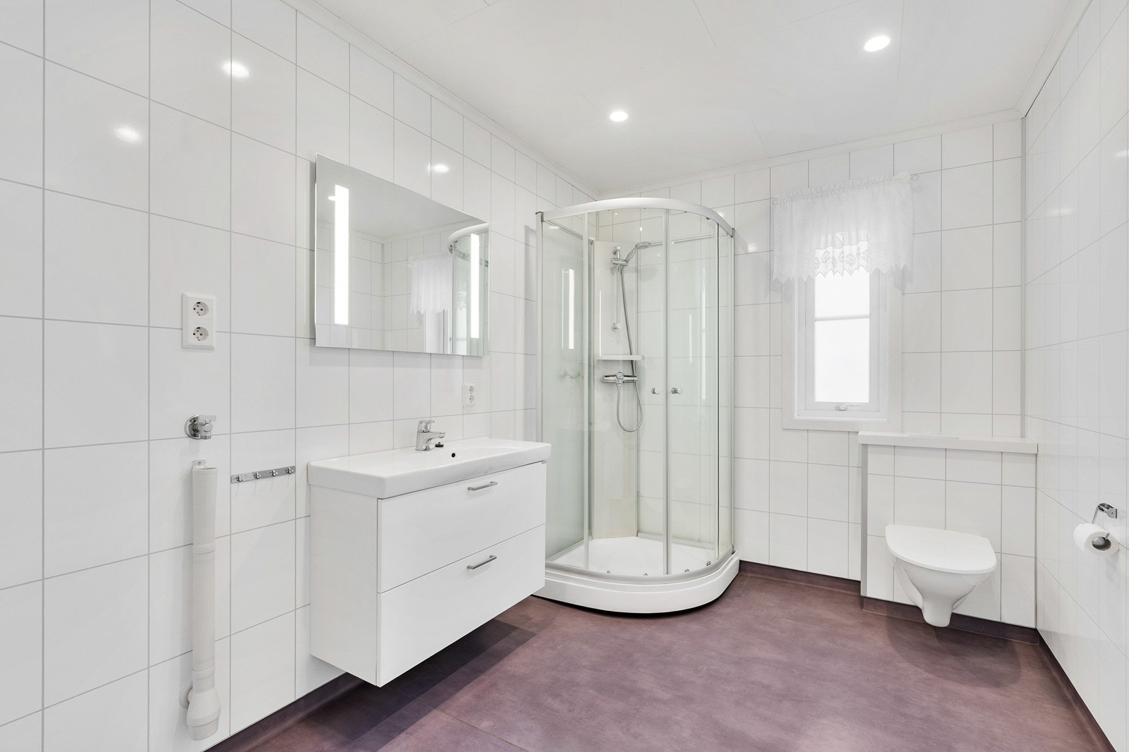 Et romslig bad med belegg på gulv med varmekabler og våtromsplater på vegger. Opplegg for vaskemaskin. Galleribilde