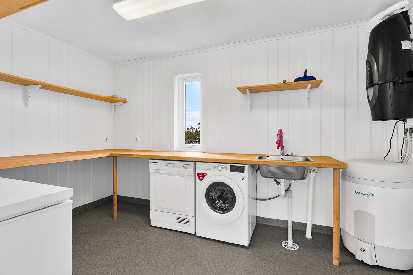 Sportsbod/teknisk rom inneholder varmtvannsbereder, ventilasjonsanlegg, sentralstøvsuger, benk med skyllekar, opplegg for vaskemaskin, vannfordelingsskap og sikringsskap. Praktiske hyller. Rommet er godkjent som teknisk rom/bod. Galleribilde