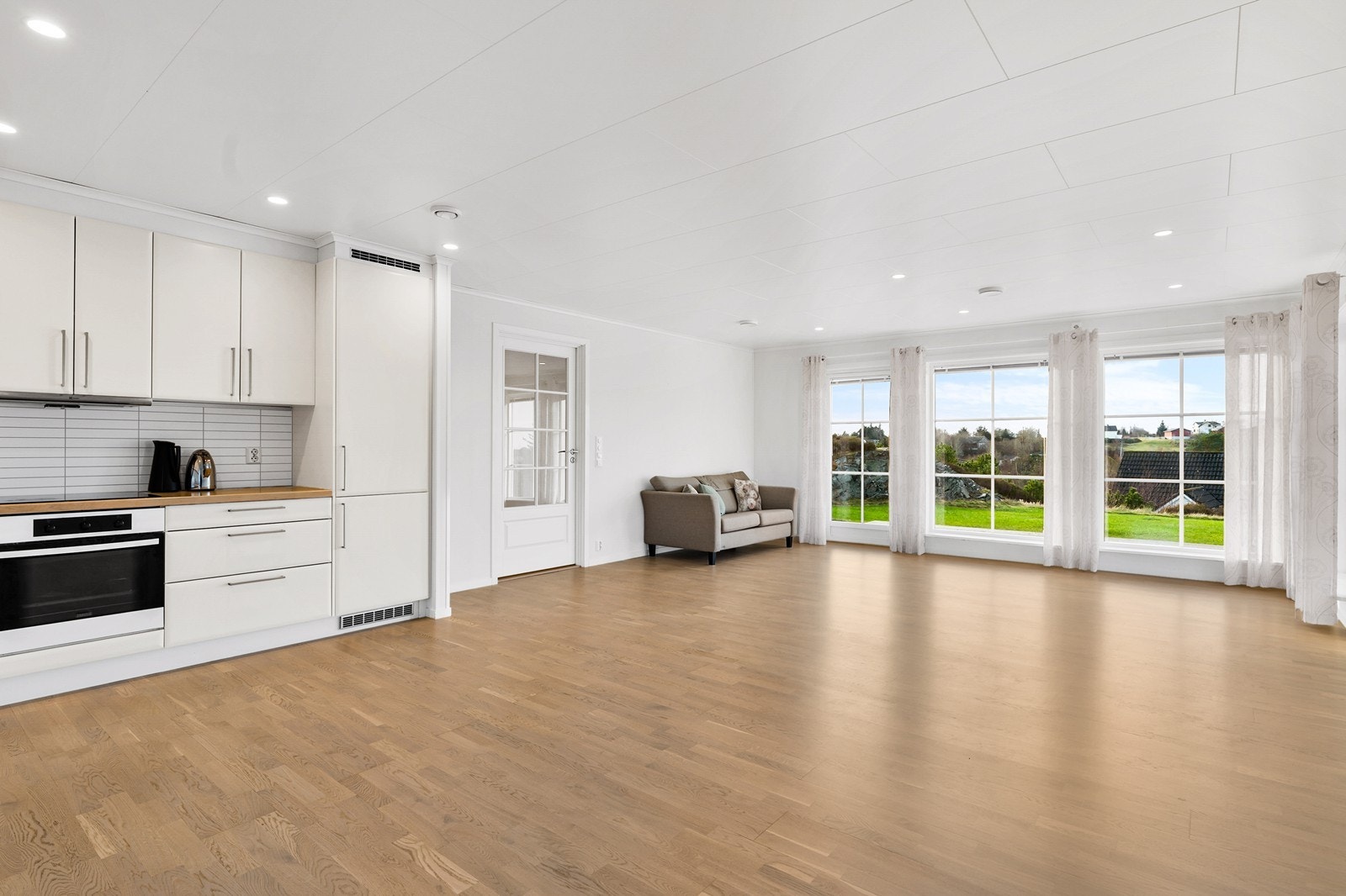 Romslig stue/kjøkken med tapetserte vegger, parkett på gulv og plater i himling med spotbelysning. Galleribilde