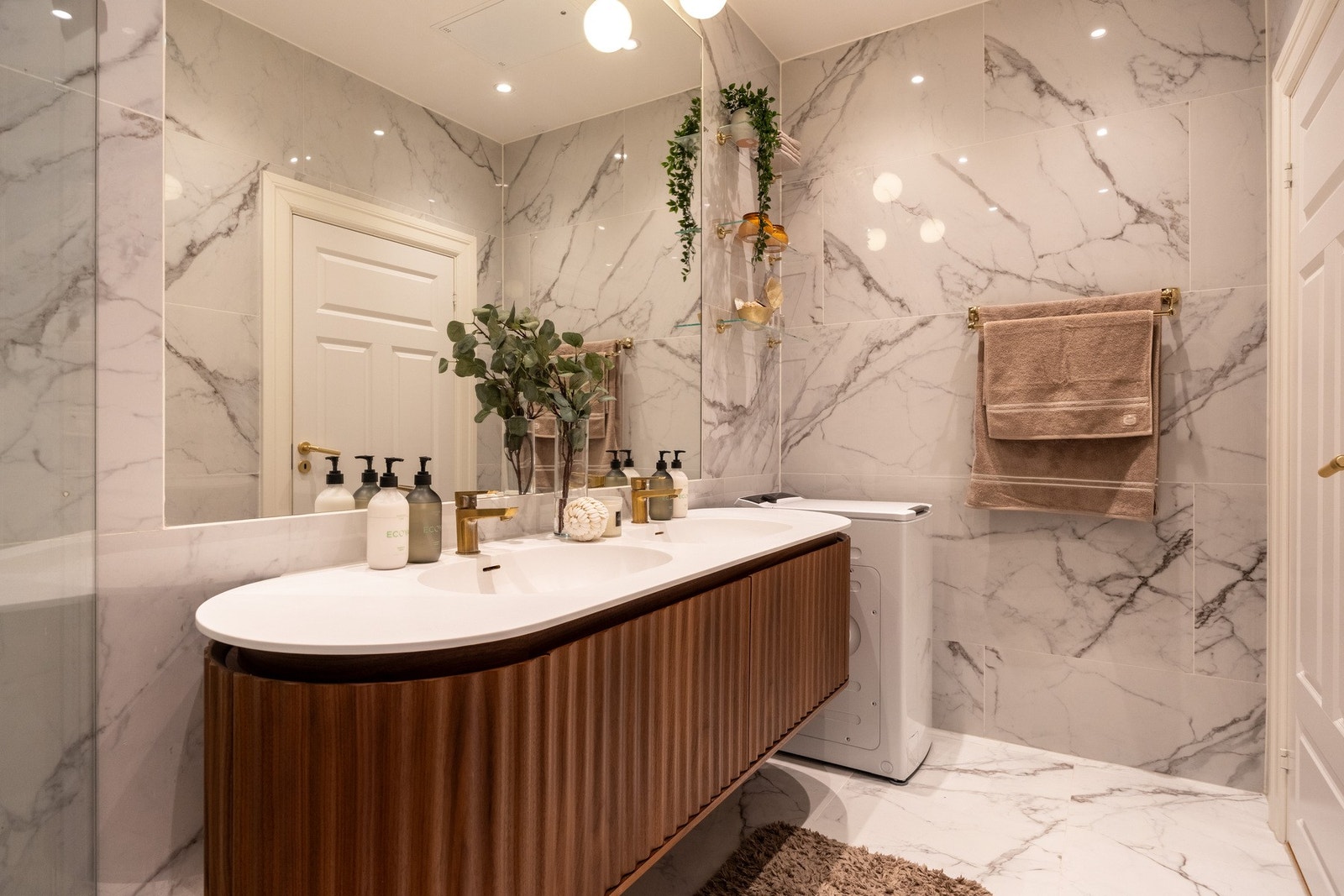 Baderomsinnredning med dobbel heldekkende servant og underskap med skuffer, dusjhjørne med innfellbare dører i herdet glass, samt veggmontert toalett. Det er opplegg og plass for vaskemaskin. Galleribilde