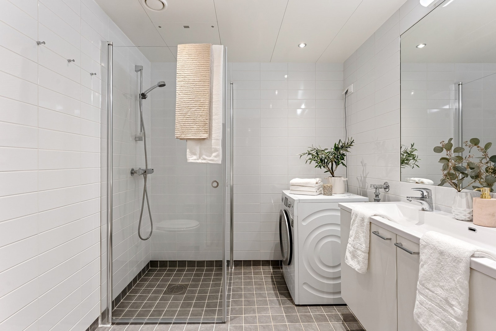 Moderne og flislagt baderom med gulvvarme, downlights i himling og opplegg for både vaskemaskin og tørketrommel Galleribilde