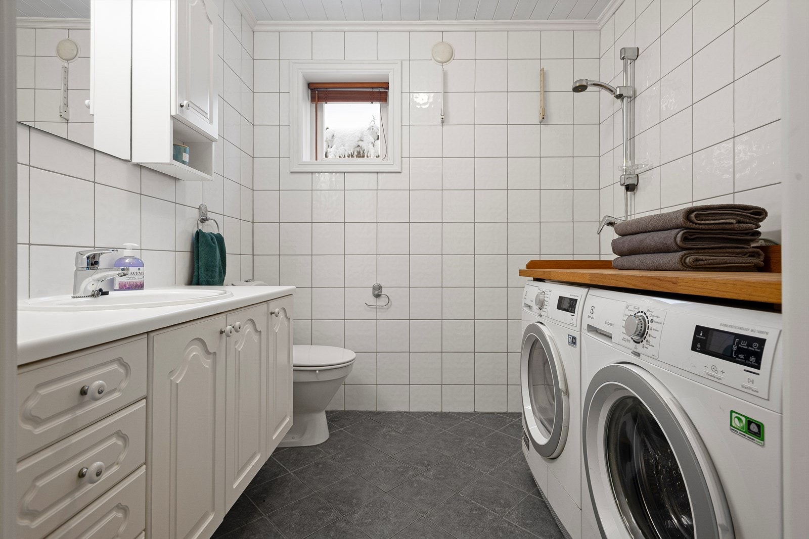 Praktisk bad i 1. etasje med benkeskap og veggskap med profilerte fronter, dusj på gulv, servant og toalett Galleribilde