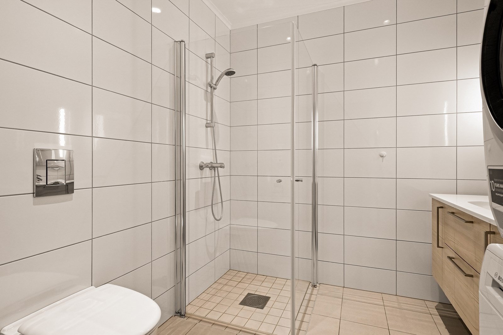 Flislagt bad med varme i gulv, opplegg til vaskemaskin, dusjhørne, vegghengt toalett og stor baderomsinnredning Galleribilde