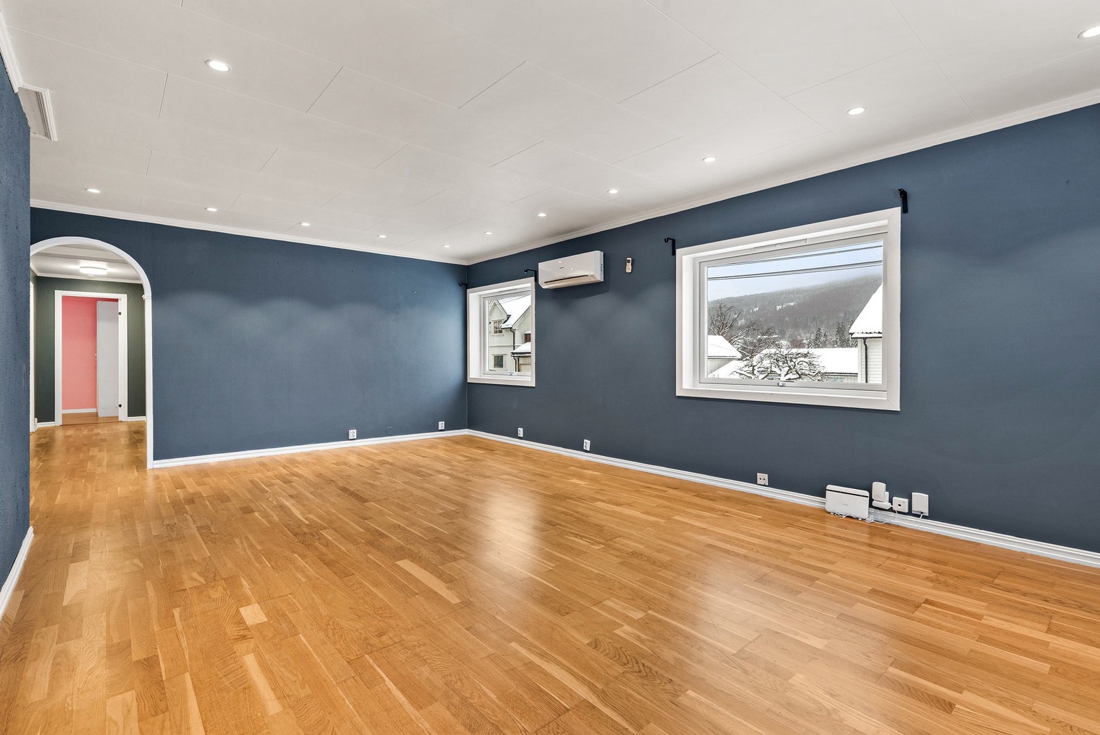 Romslig stue med 3-stavs parkettgulv, slette flater på vegger og takessplater samt downlights i himling Galleribilde