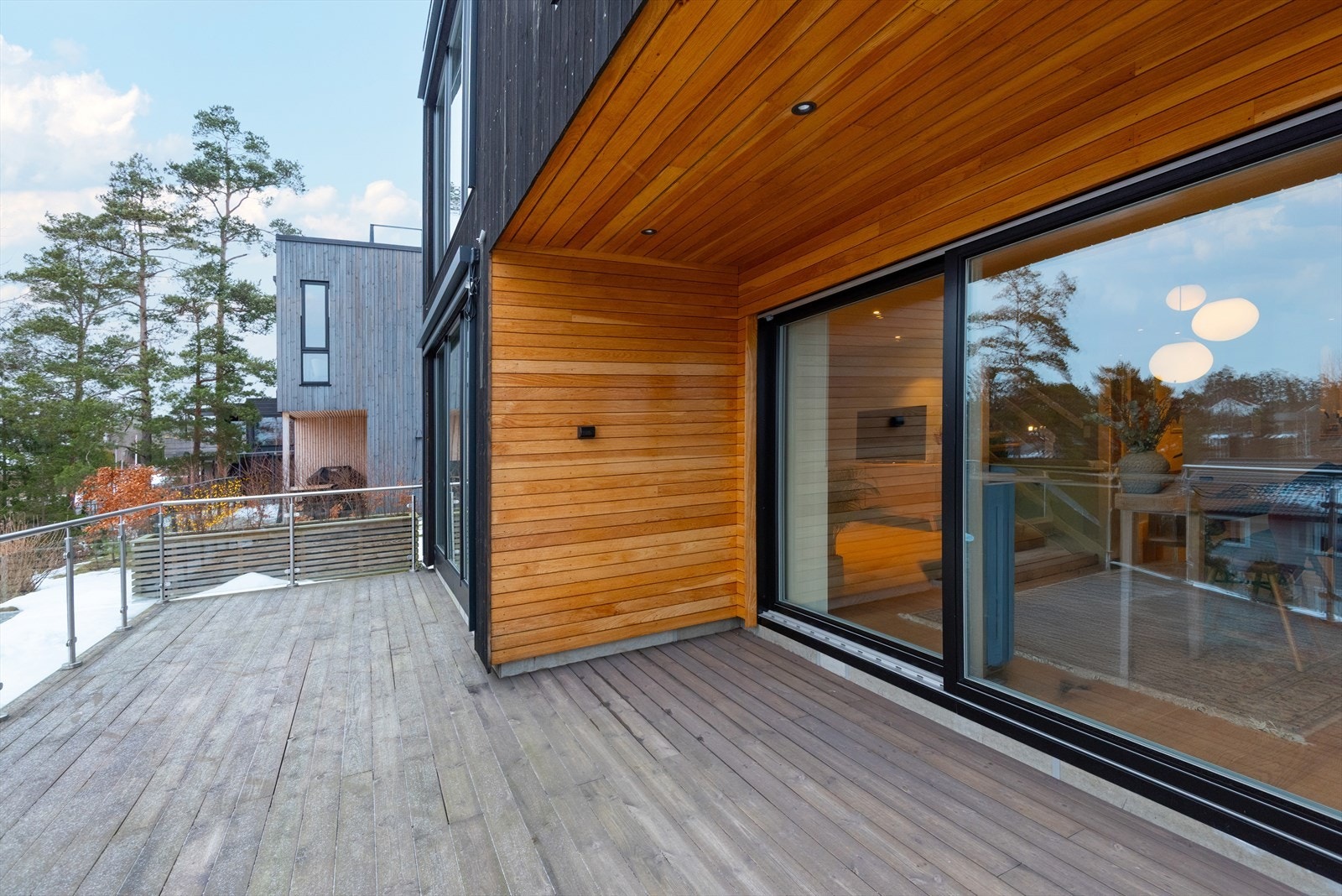 Terrassen nås enkelt fra tre sider av boligen, blant annet direkte fra spisestuen. Terrassen har moderne rekkverk i stål og glass. Galleribilde