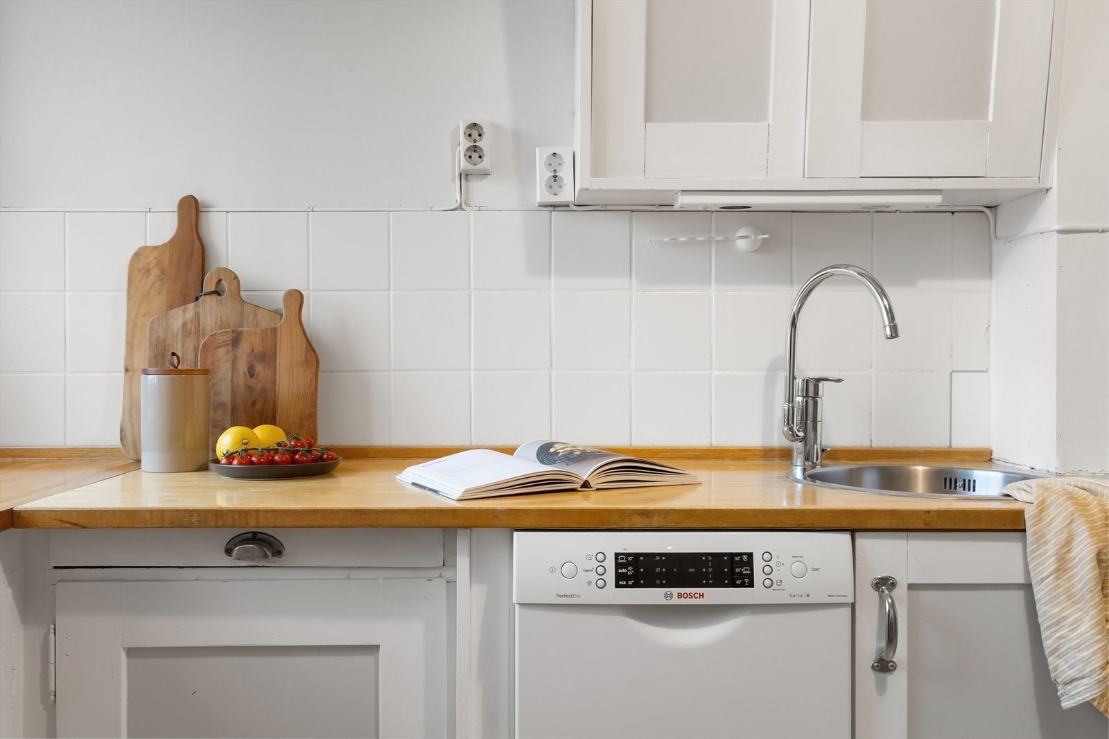 Kjøkkenet har profilerte fronter, heltre benkeplate med nedfelt vaskekum, fliser over benkeplaten og opplegg for oppvaskmaskin. Galleribilde