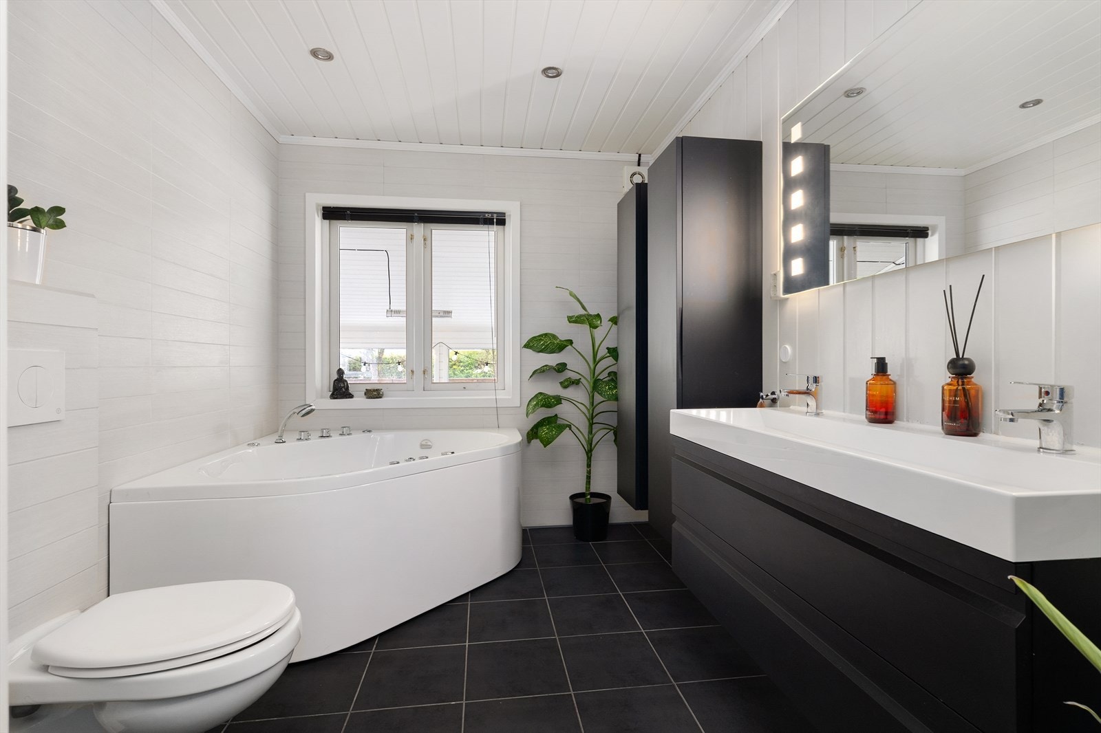 Badet er renovert i 2011, med murt gulv og tilhørende elektroarbeider. Rommet er innredet med badekar, veggmontert toalett, dusjkabinett og servantinnredning med skuffer og speil med lys. Galleribilde