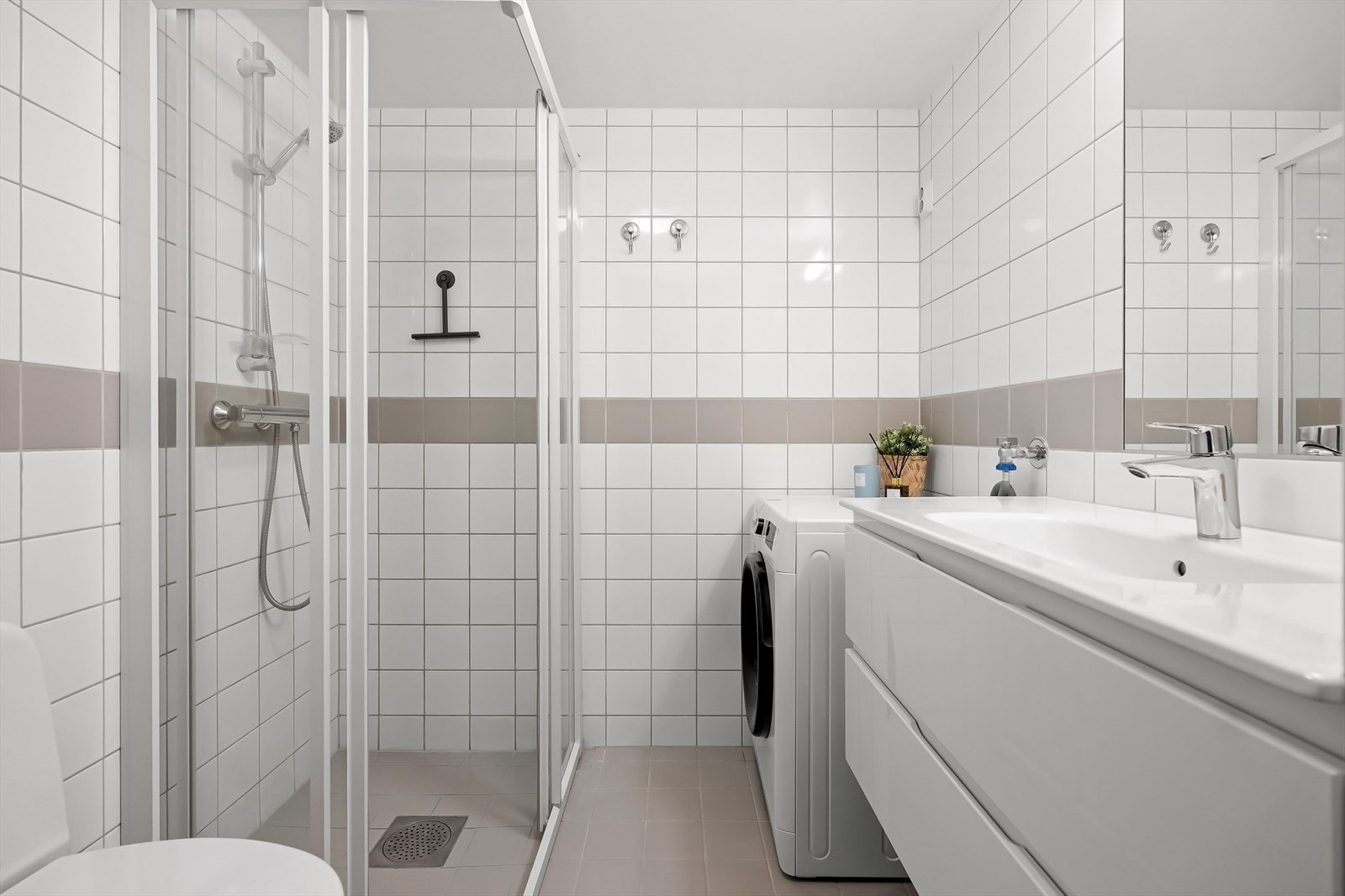 Romslig bad med dusjhjørne, wc, servant med skuffer, speil og opplegg for vaskemaskin. Galleribilde