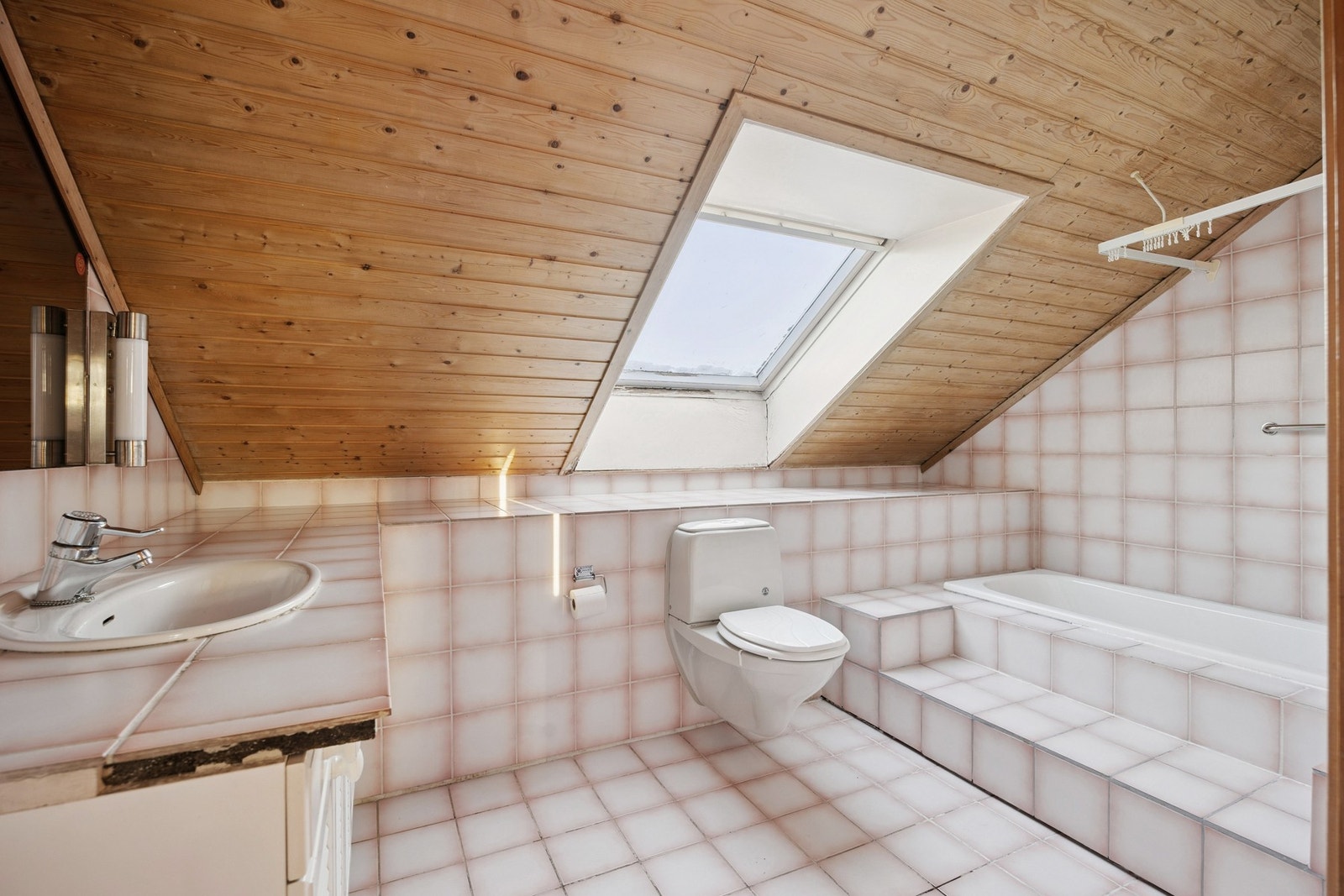 Badet i loftsetasjen har flislagt gulv og vegger og inneholder badekar med innebygget armatur, servantinnredning med ovenpåliggende servant, speil med sidelys, vegghengt høyskap og vegghengt toalett. Galleribilde